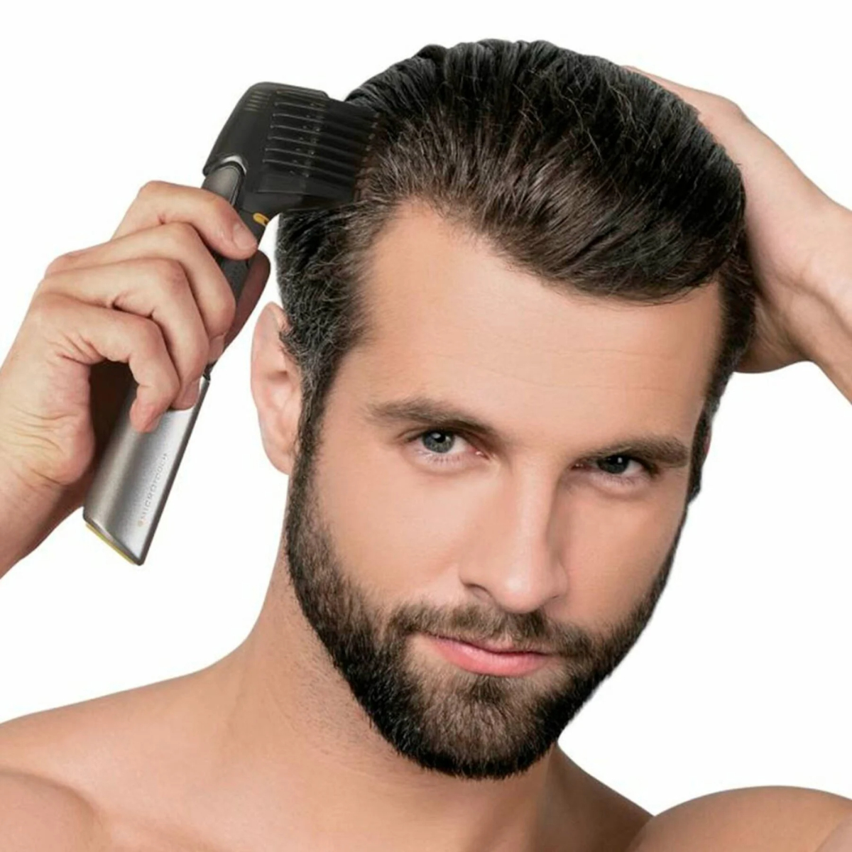 Un hombre usando una recortadora de cabello en su cabello. Está mirando a la cámara.