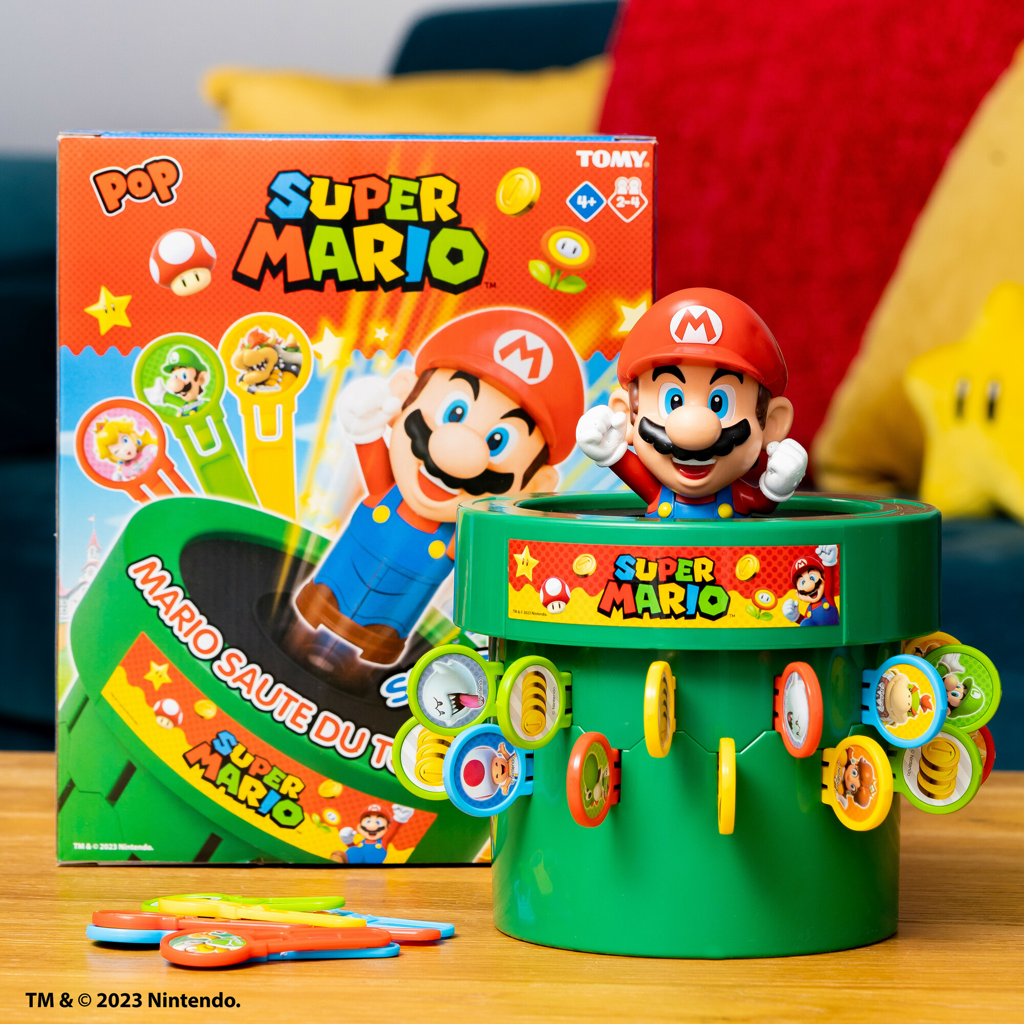 Un gioco da tavolo di Super Mario con una figura che esce da un tubo verde, pezzi del gioco e scatola sullo sfondo.