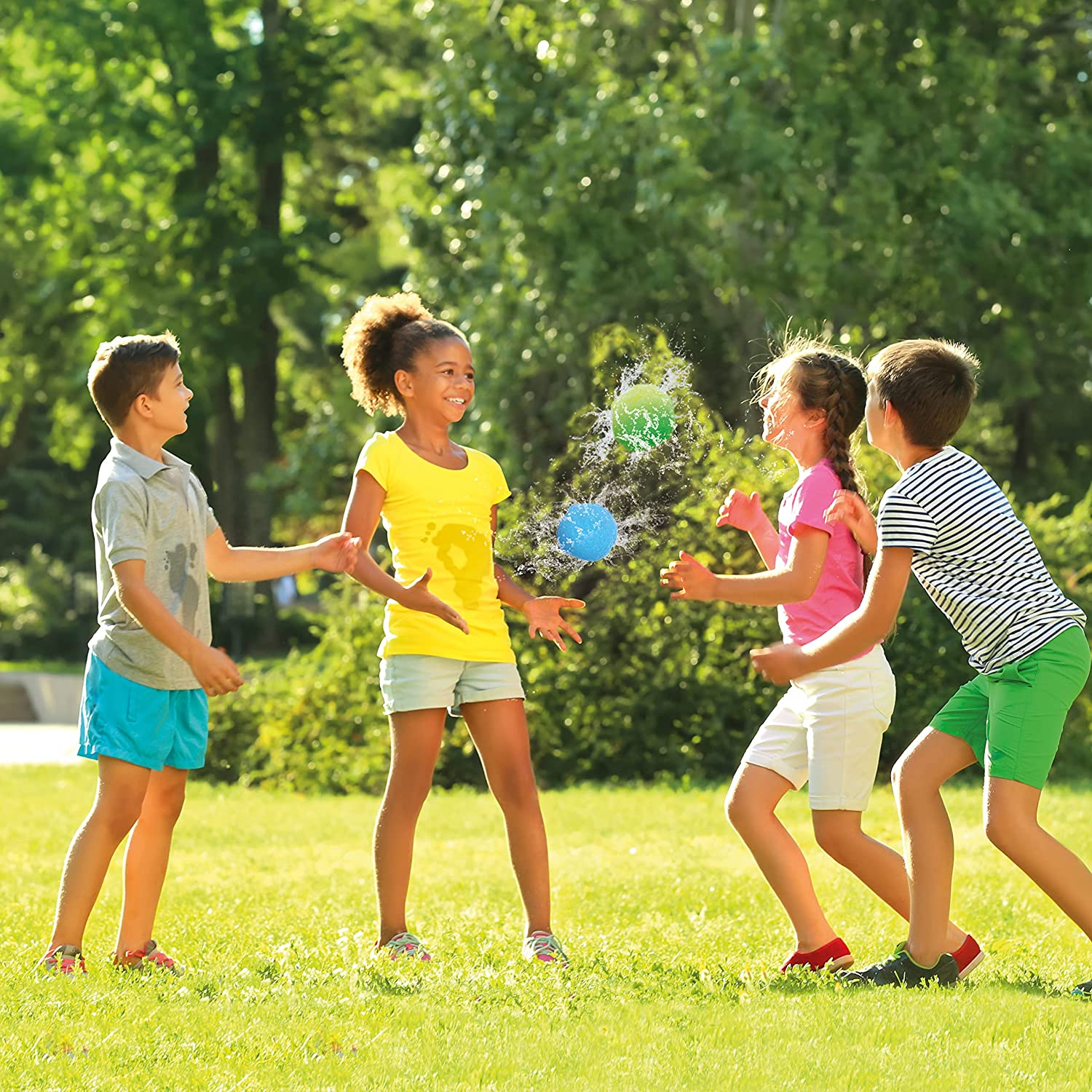 Vier Kinder spielen Wasserballon-Werfen auf Gras. Ein Kind fängt gerade einen blauen Ballon.