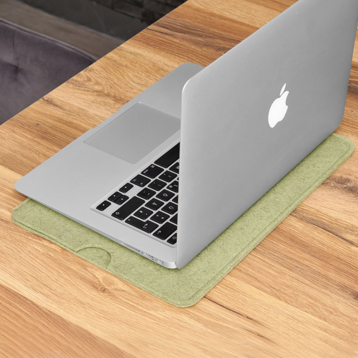 Silbernes MacBook auf einem Holztisch. Ein grünes Filzpad unter dem Laptop ist sichtbar.