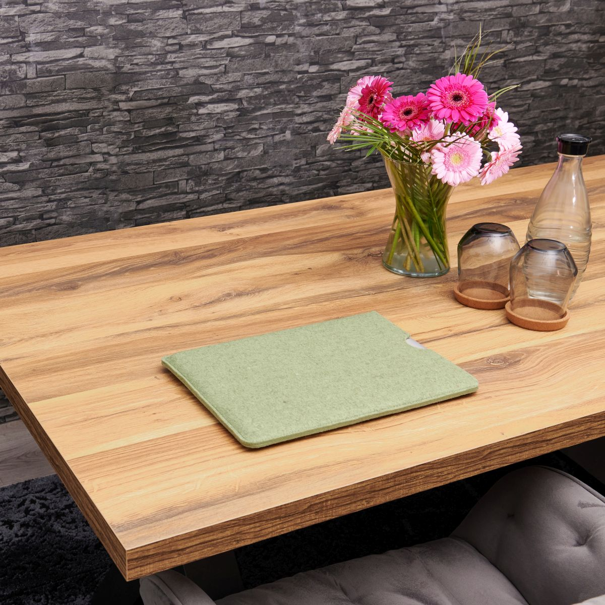 Holztisch mit grünem Filzpad, Vase mit rosa Blumen und klaren Flaschen.
