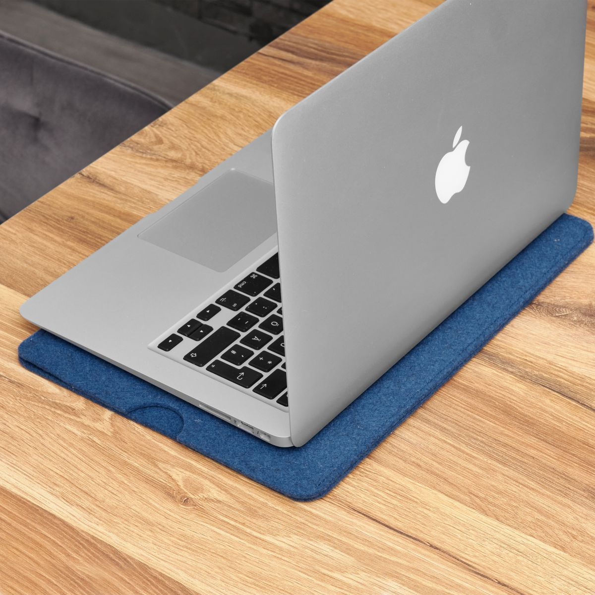 Ein silberner Laptop auf einem Holztisch mit einem blauen Filzpad darunter.