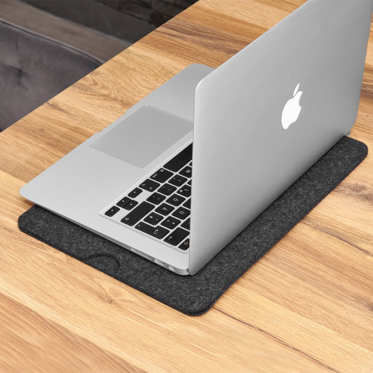 Laptop auf Holztisch, auf Filzunterlage. Apple-Logo sichtbar.