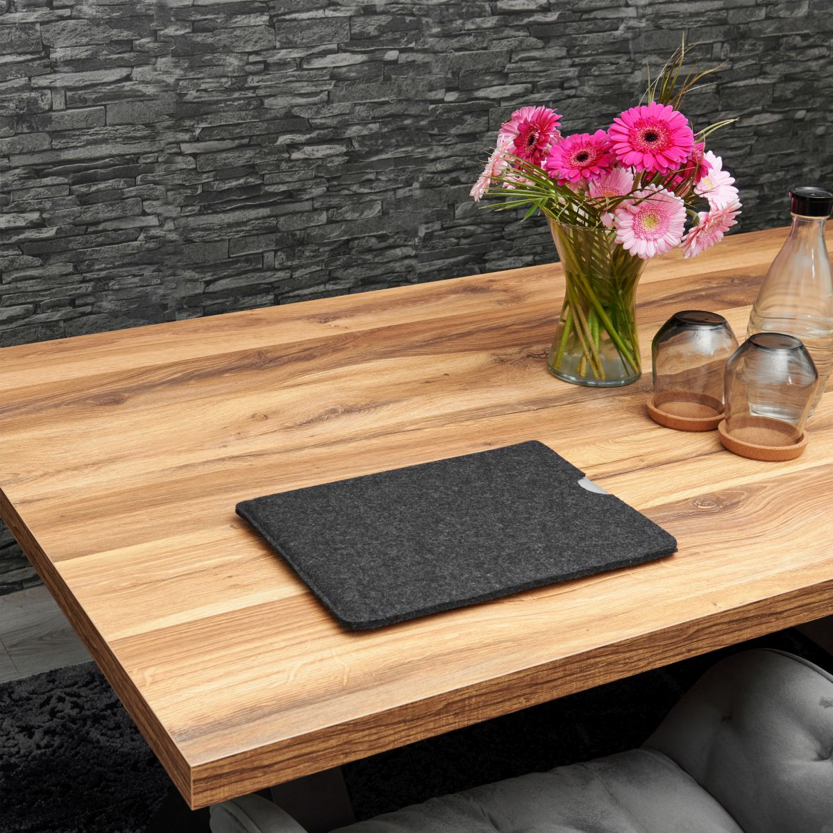 Holztisch mit Blumen und Gläsern. Eine dunkelgraue Filzhülle liegt darauf.