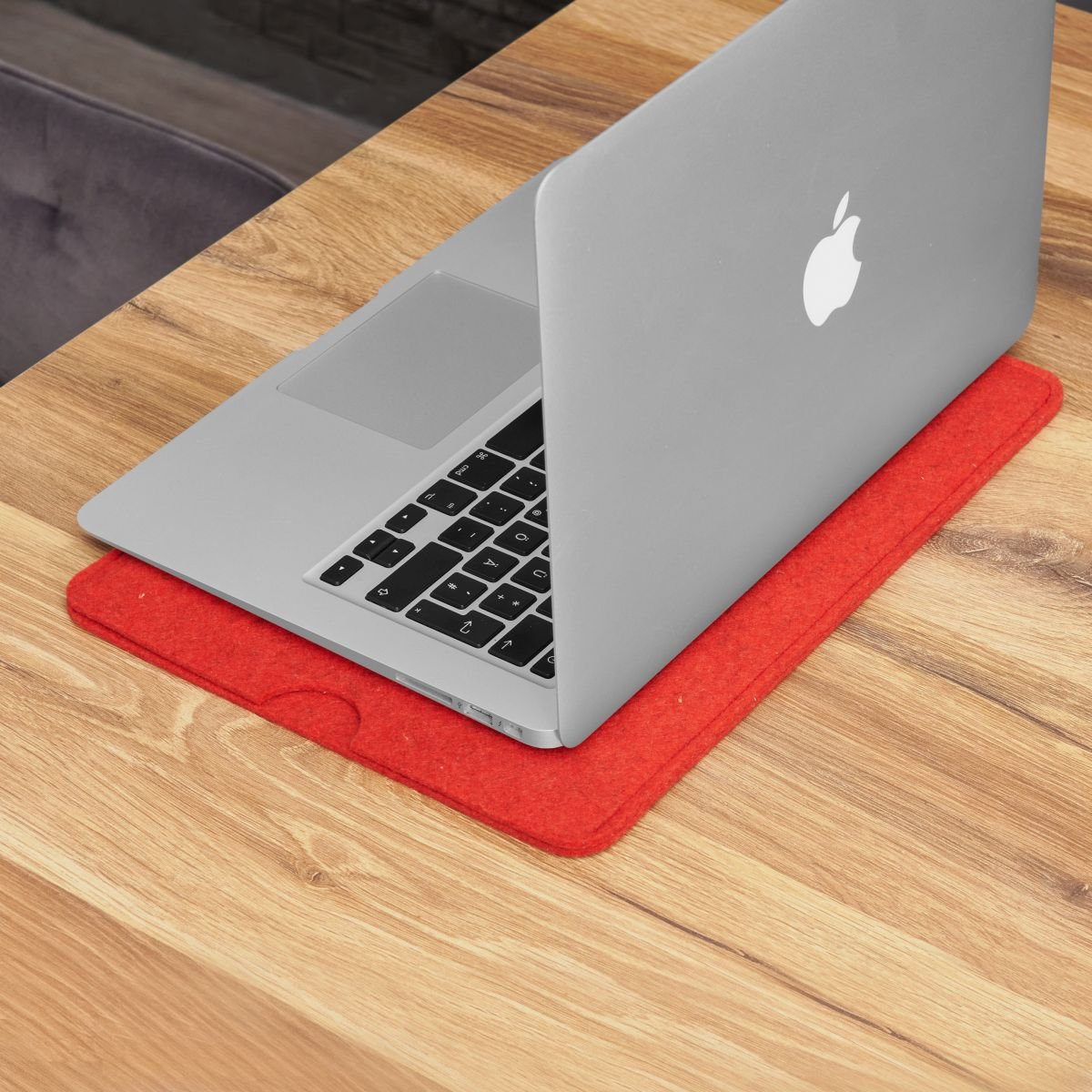 Laptop auf rotem Filzpad auf Holztisch. Apple-Logo sichtbar.