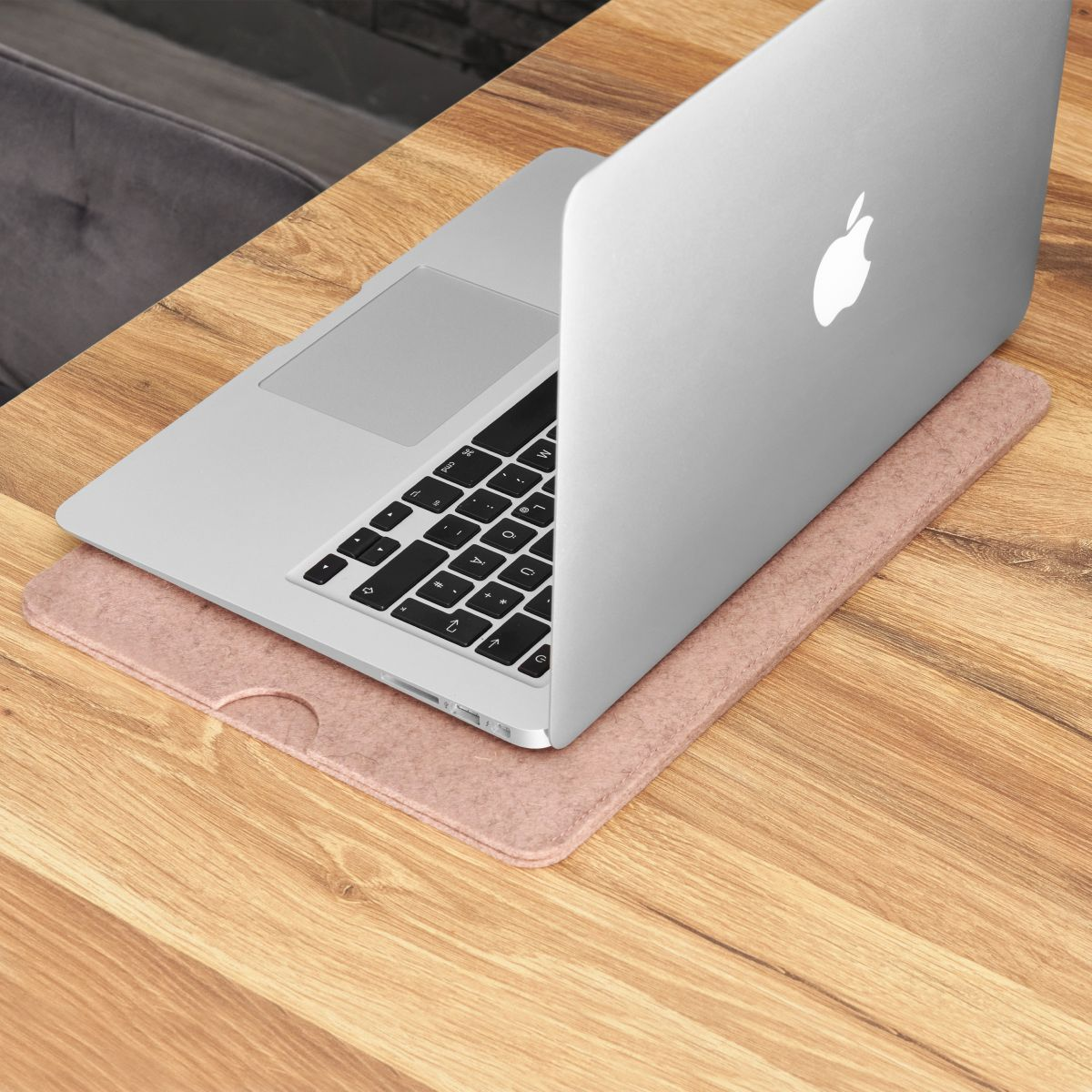 Ein silberner Laptop auf einem rosa Filzpad auf einem Holztisch. Ein Teil des Holzes ist sichtbar.