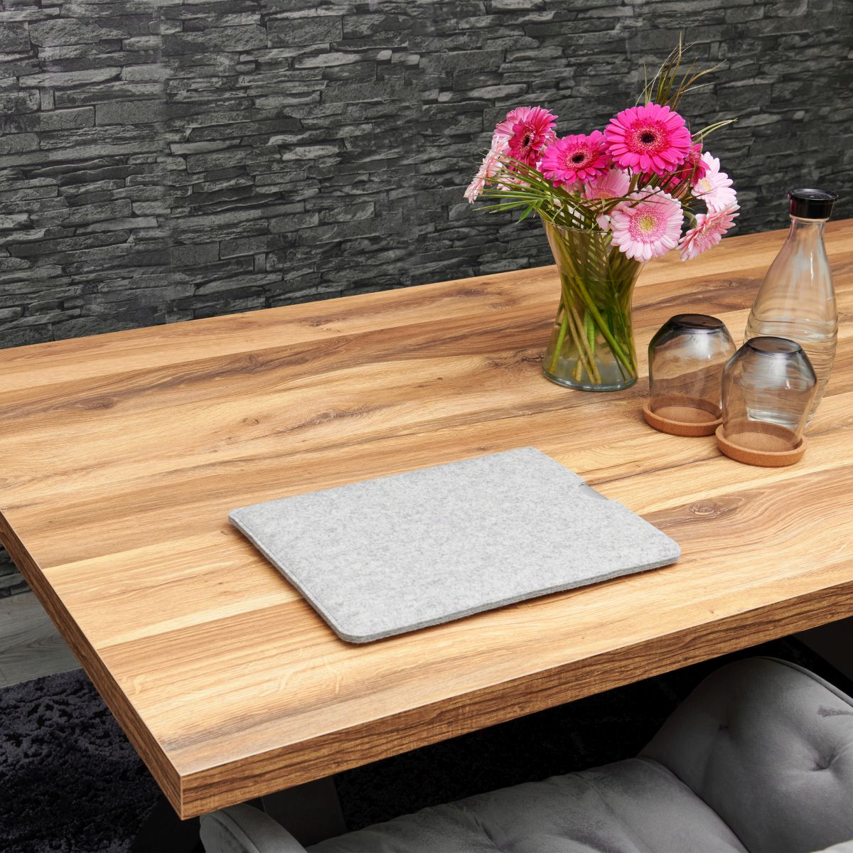 Holztisch mit Blumen in einer Vase, einer grauen Filzhülle und einer Flasche und Gläsern.