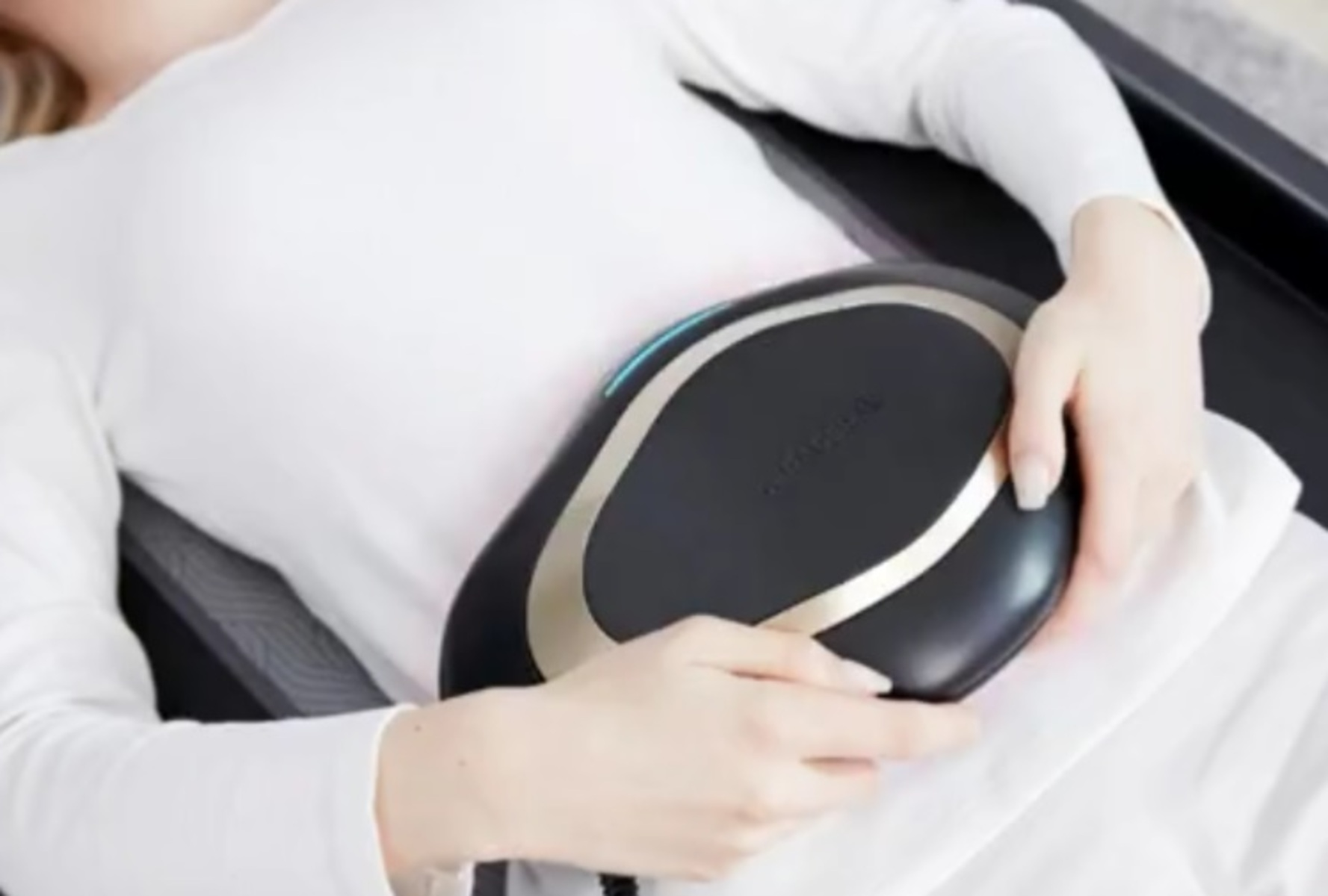 Frau benutzt ein schwarz-goldenes medizinisches Gerät auf ihrem Bauch, weißer Hintergrund.
