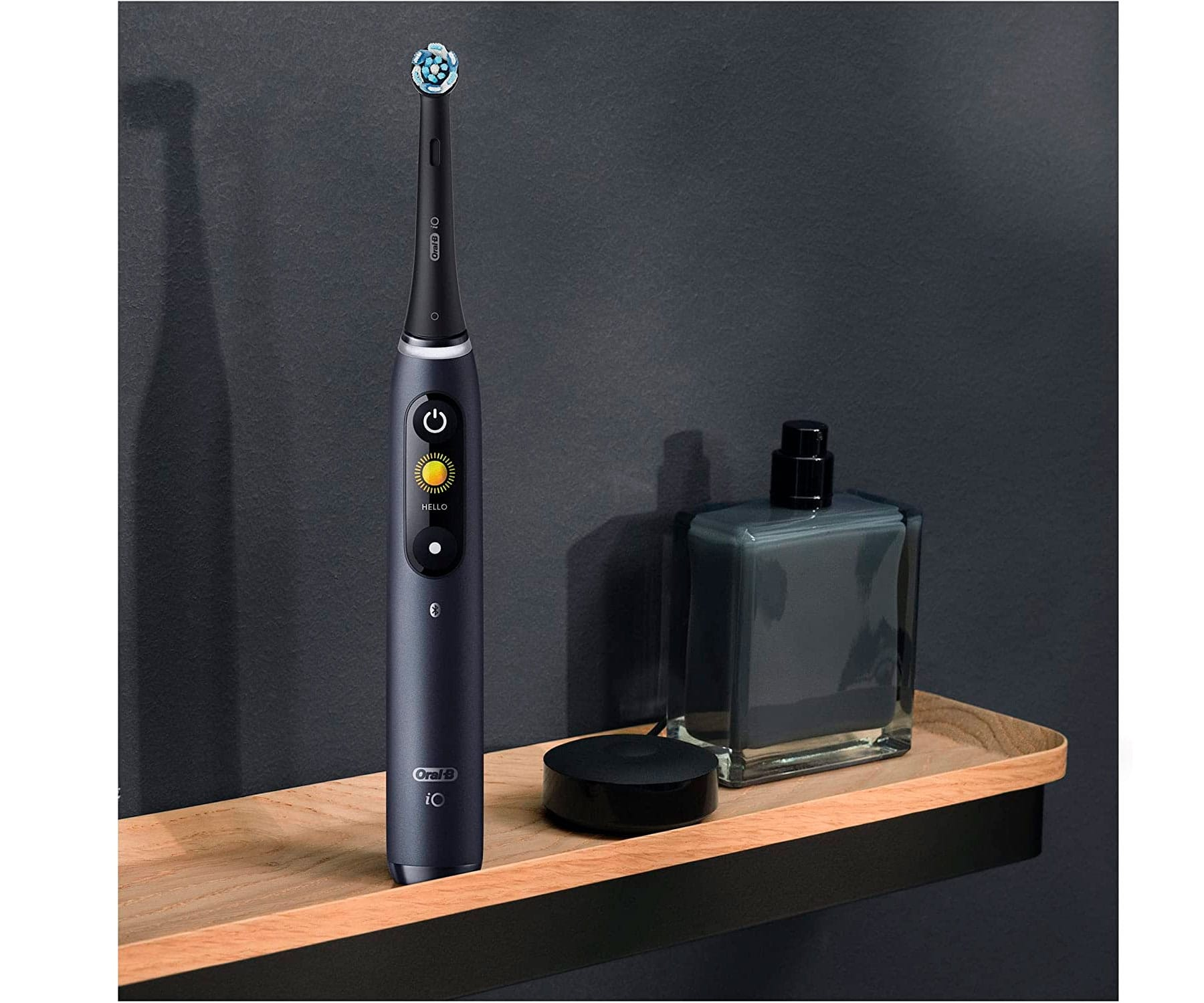 Elektryczna szczoteczka do zębów na półce, z butelką perfum, na tle ciemnoszarej ściany.