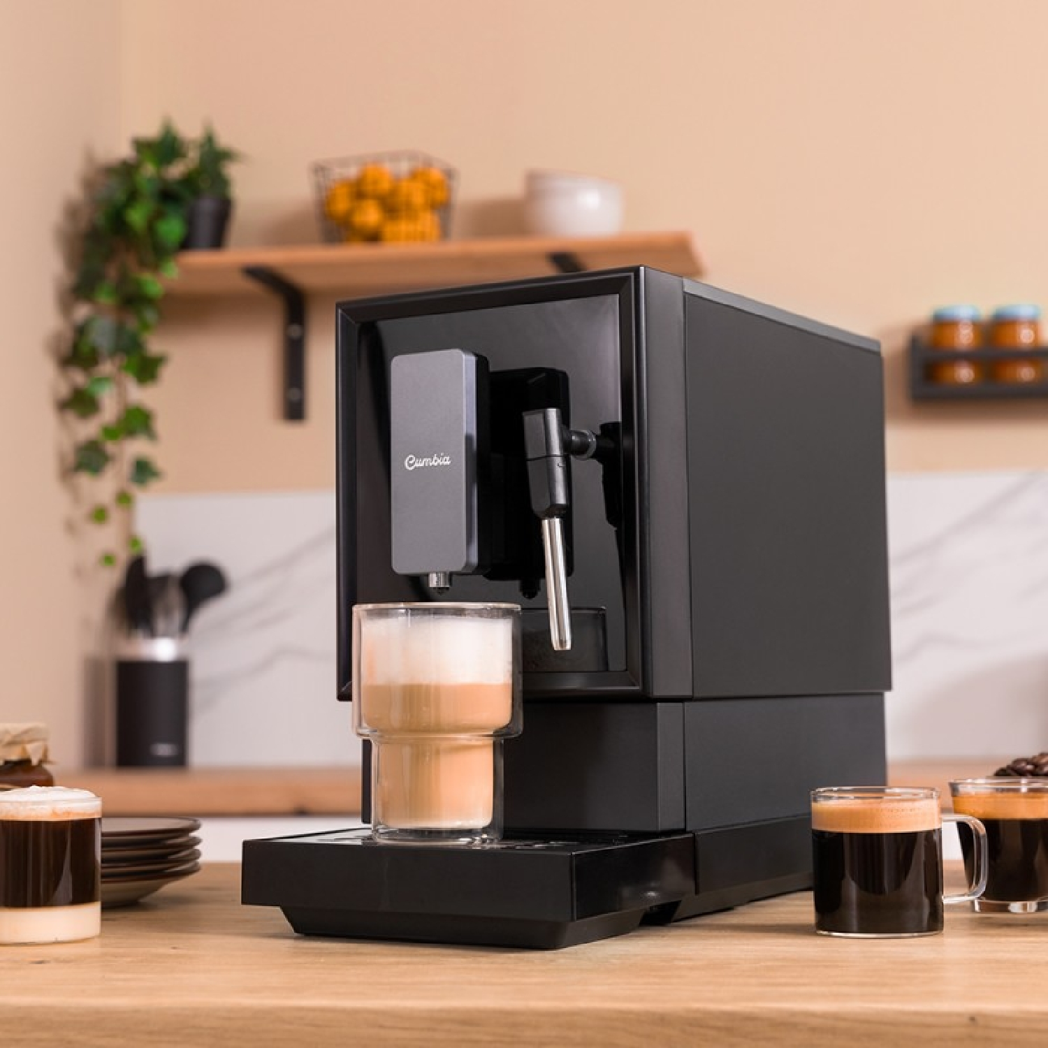 Máquina de espresso negra con un vaso de café delante, sobre una encimera de madera.