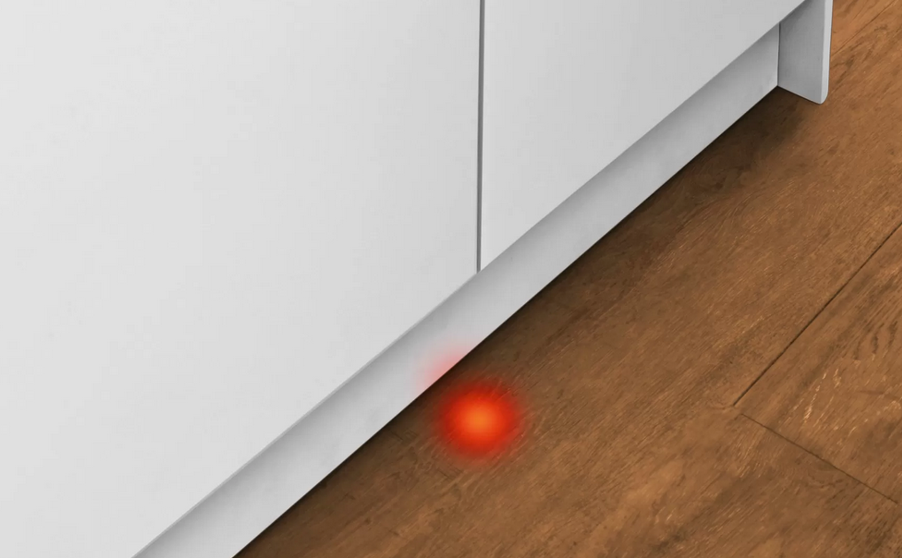 Ein rot leuchtendes Licht auf dem Boden in der Nähe eines weißen Schranks.