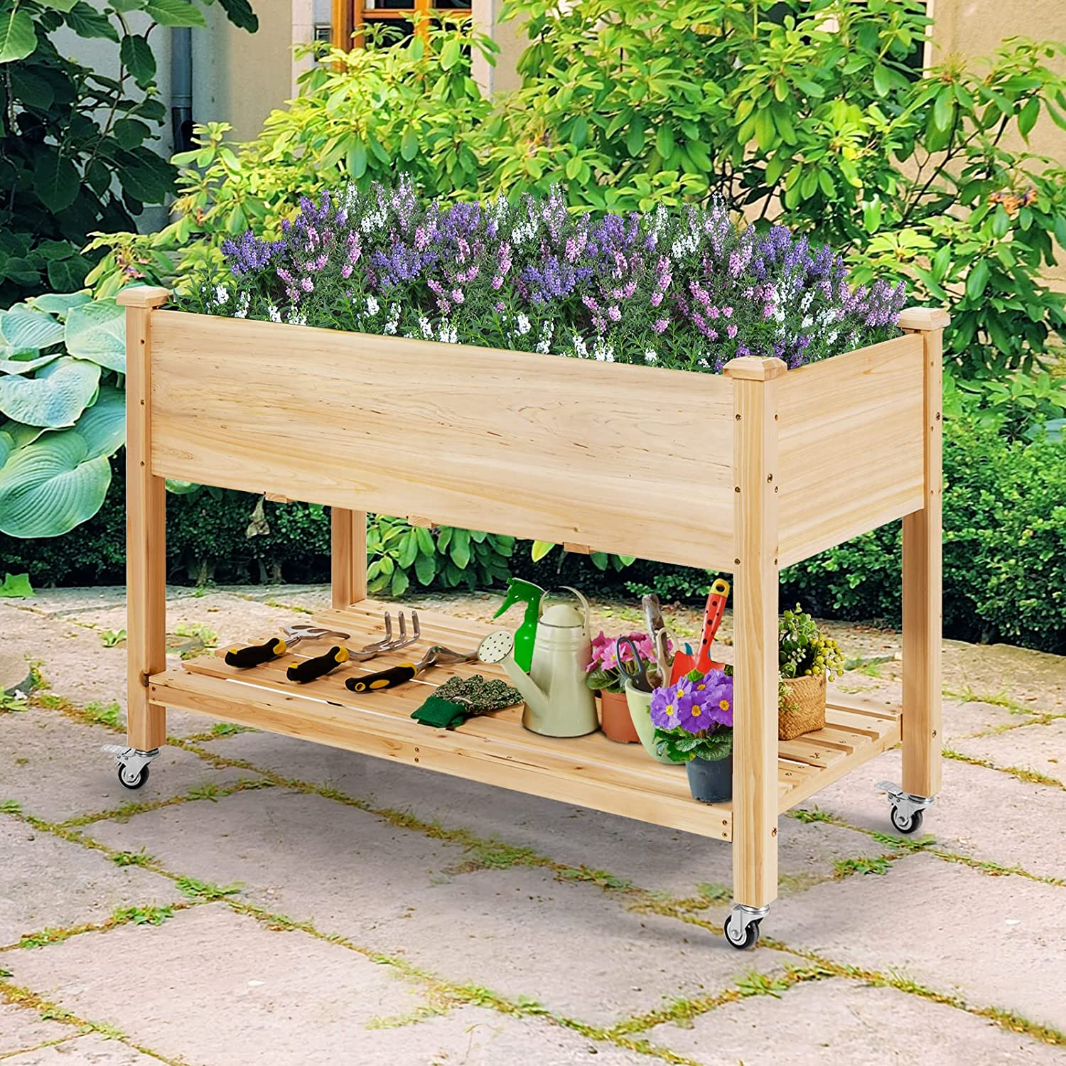 Erhöhtes Gartenbeet aus Holz mit Blumen, Werkzeugen und Pflanzen auf einem unteren Regal. Räder sichtbar.