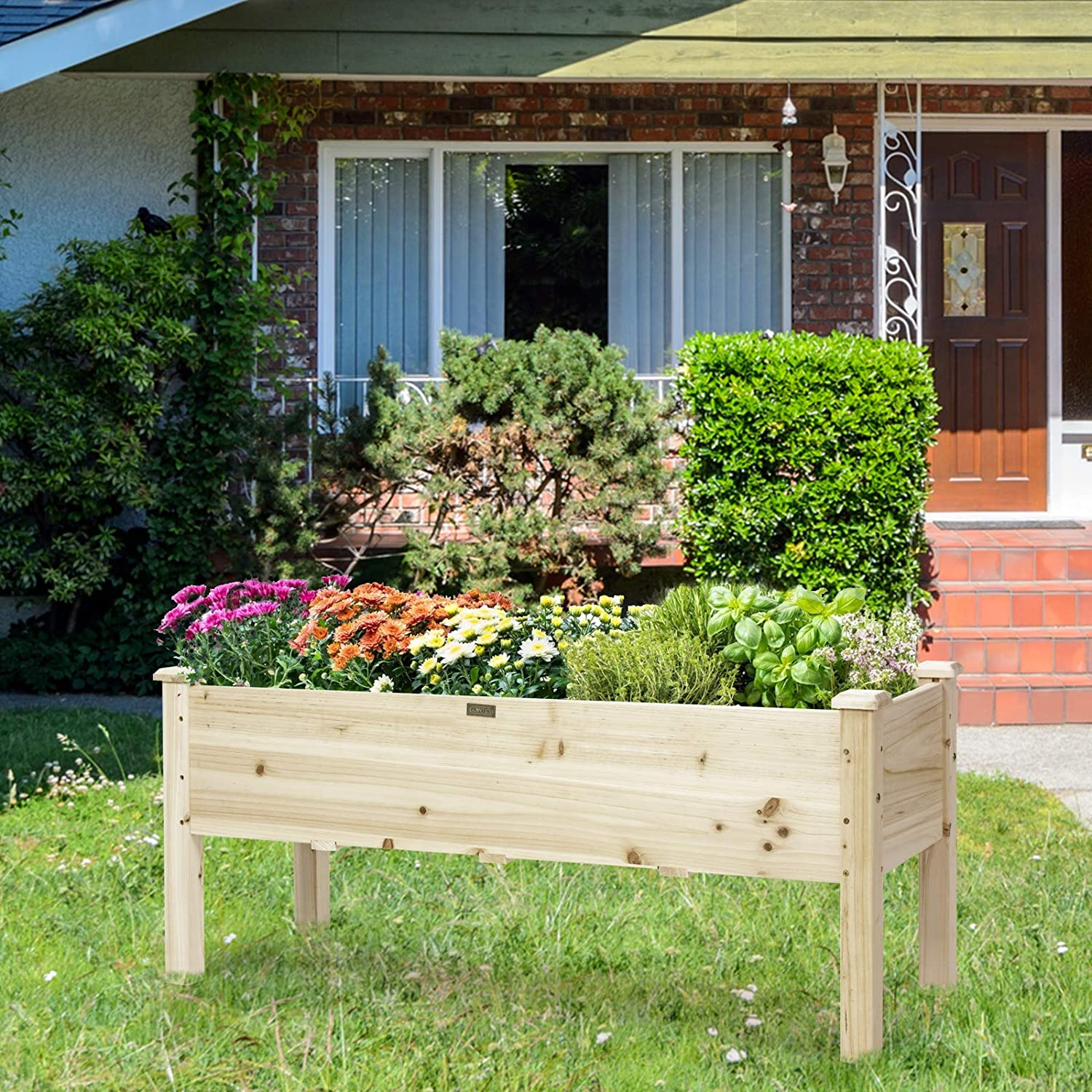 Ein erhöhter Gartenbeet aus Holz mit Blumen und Pflanzen, vor einem Haus.