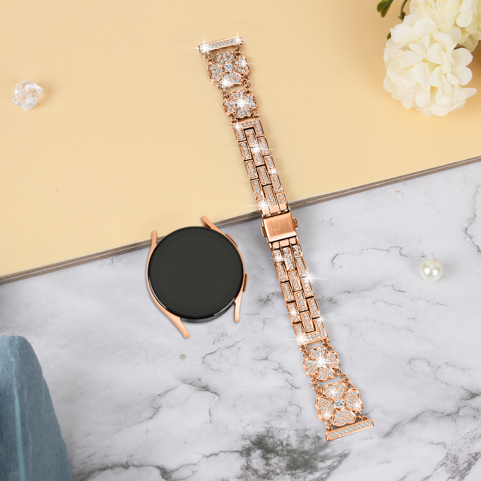 Roségoldene Uhr und Armband mit floralem Design, diamantähnlichen Steinen, auf Marmor- und beigem Untergrund.
