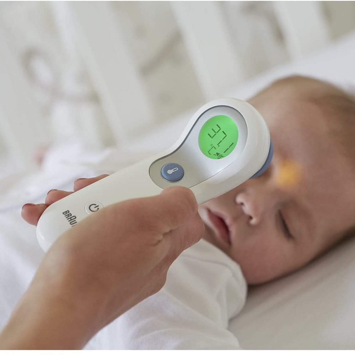 Osoba mierząca temperaturę dziecka. Używa białego termometru Braun.