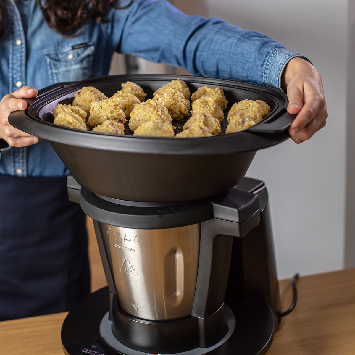 Kobieta trzyma czarną miskę z jedzeniem w kuchni. Poniżej znajduje się czarna maszyna.