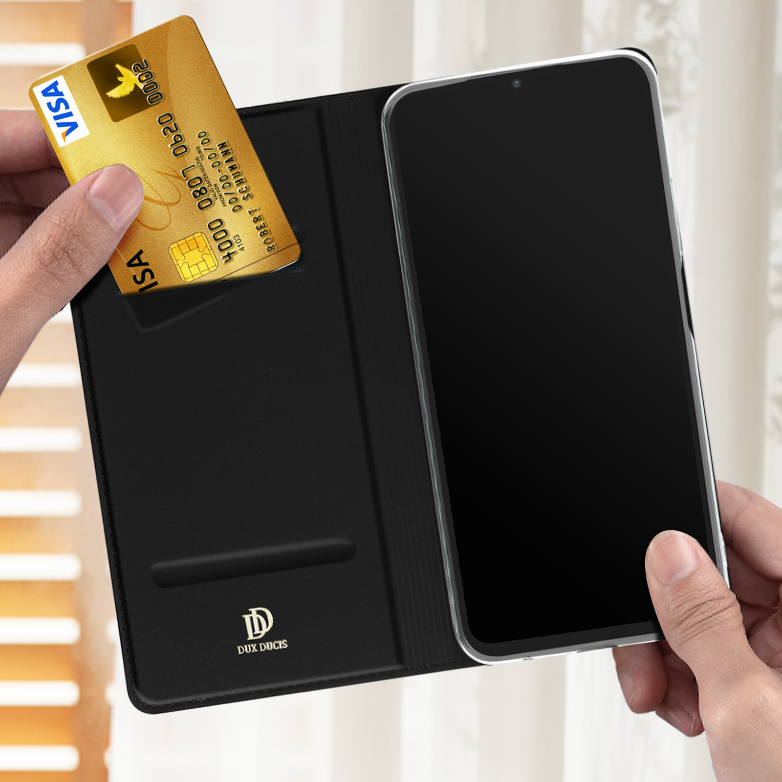 Una mano che tiene una carta di credito Visa e un telefono all'interno di un portafoglio nero.