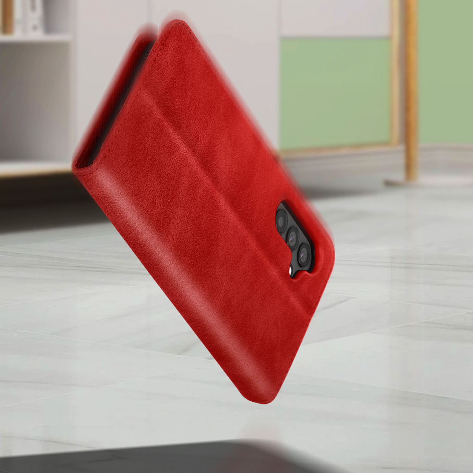 Een rode telefoonhoes valt. Het heeft een cameragedeelte. De achtergrond is wazig en grijs.
