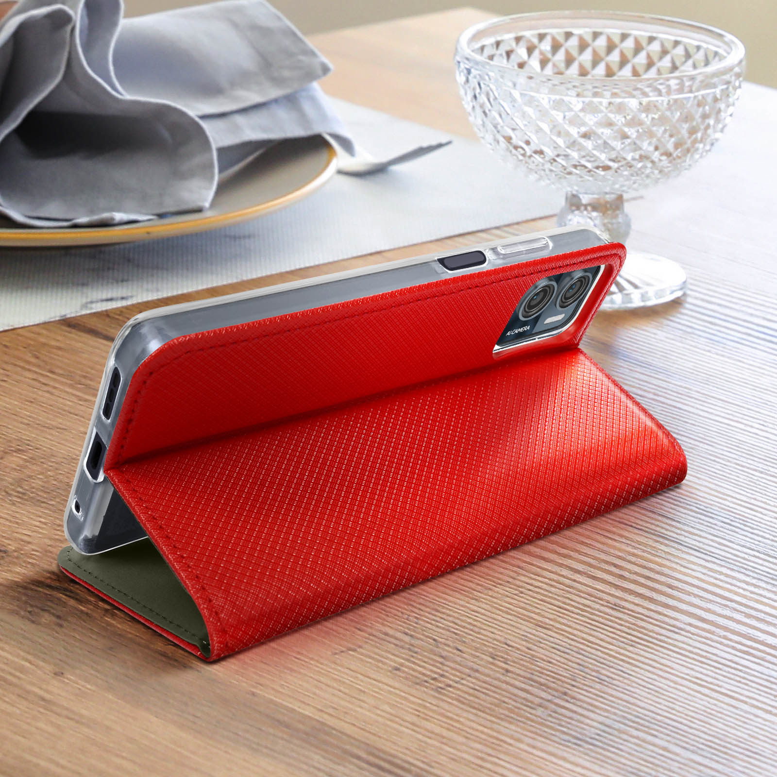 Rotes Telefonetui offen auf einem Tisch, mit Telefon darin, in der Nähe einer Glasschale und Serviette.