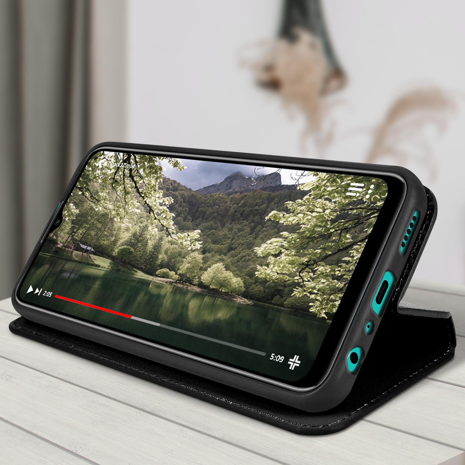 Een telefoon in een zwart hoesje, speelt een video met een meer en bomen af.