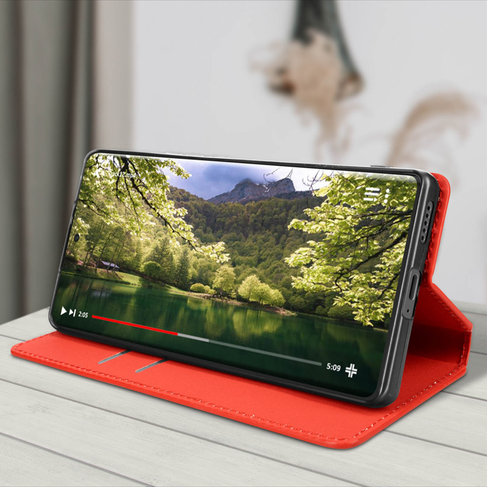 Een smartphone in een rode hoes, met een natuurvideo op een houten tafel.