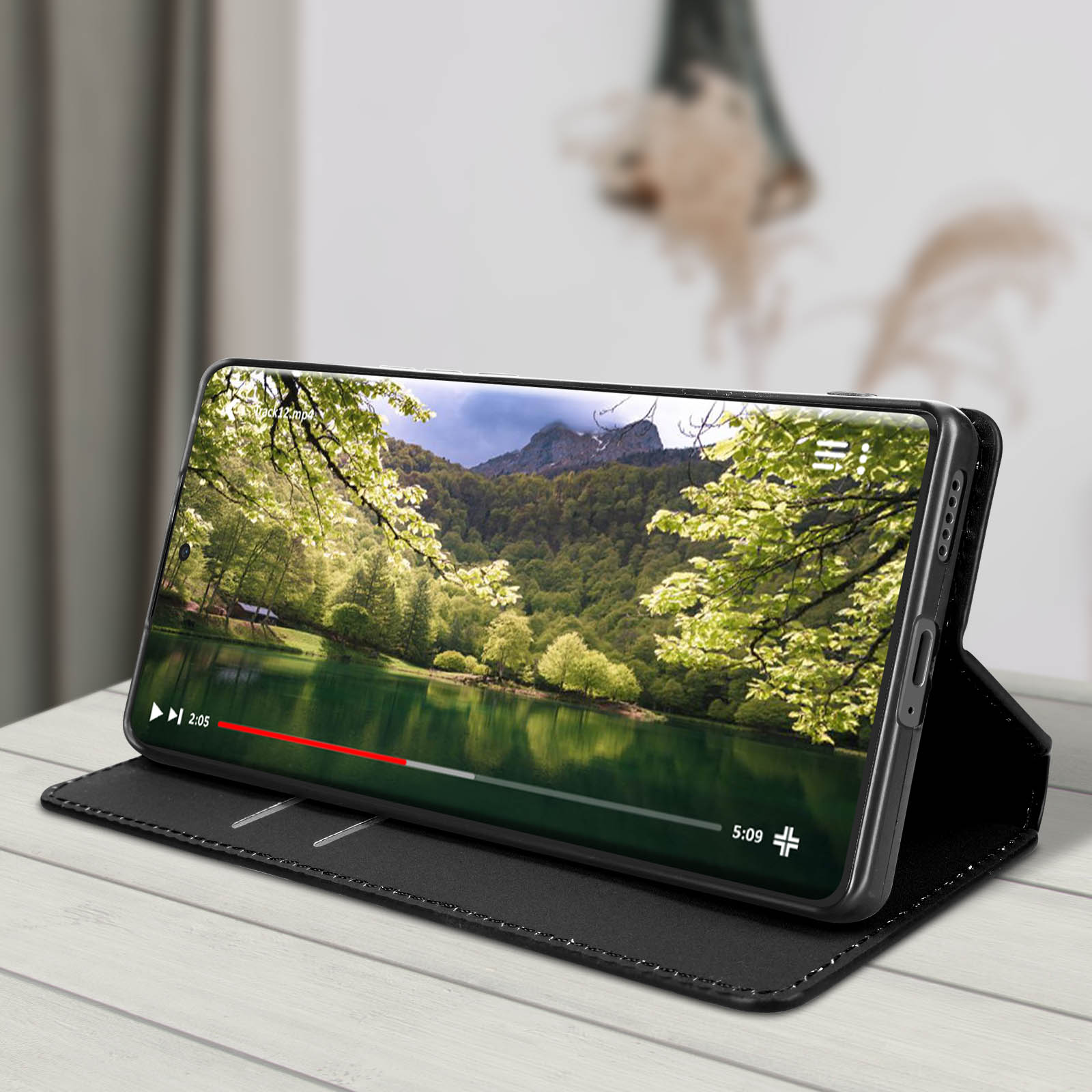 Telefono che mostra un video di un lago, in una custodia nera su una superficie di legno.