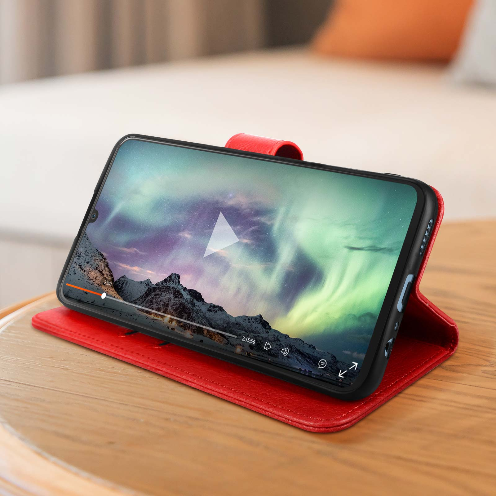 Smartphone spielt Video auf roter Hülle ab. Bildschirm zeigt Landschaft mit Bergen und Nordlichtern.