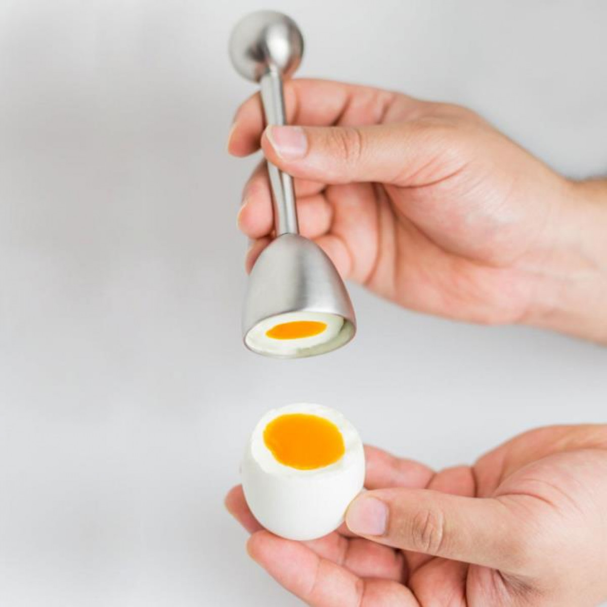 A person holding a metal egg separator over a halved boiled egg.