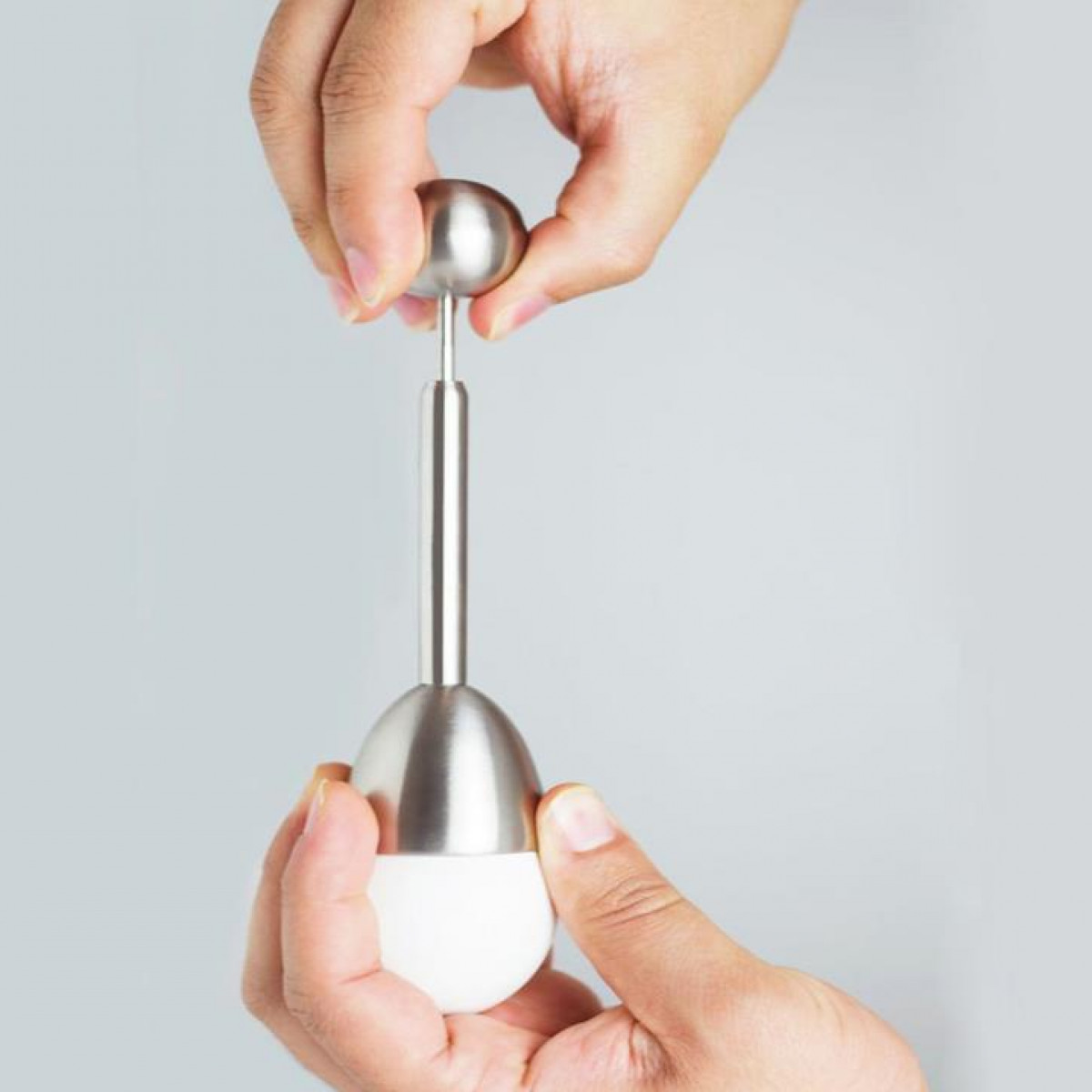 Hands using an egg separator. The separator is silver with a white egg in the bottom.