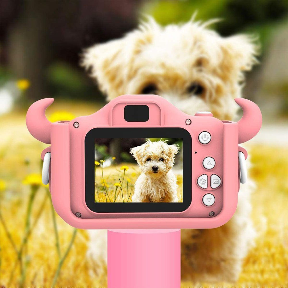 Cámara de juguete rosa con un perro pequeño en la pantalla y un perro borroso en el fondo.