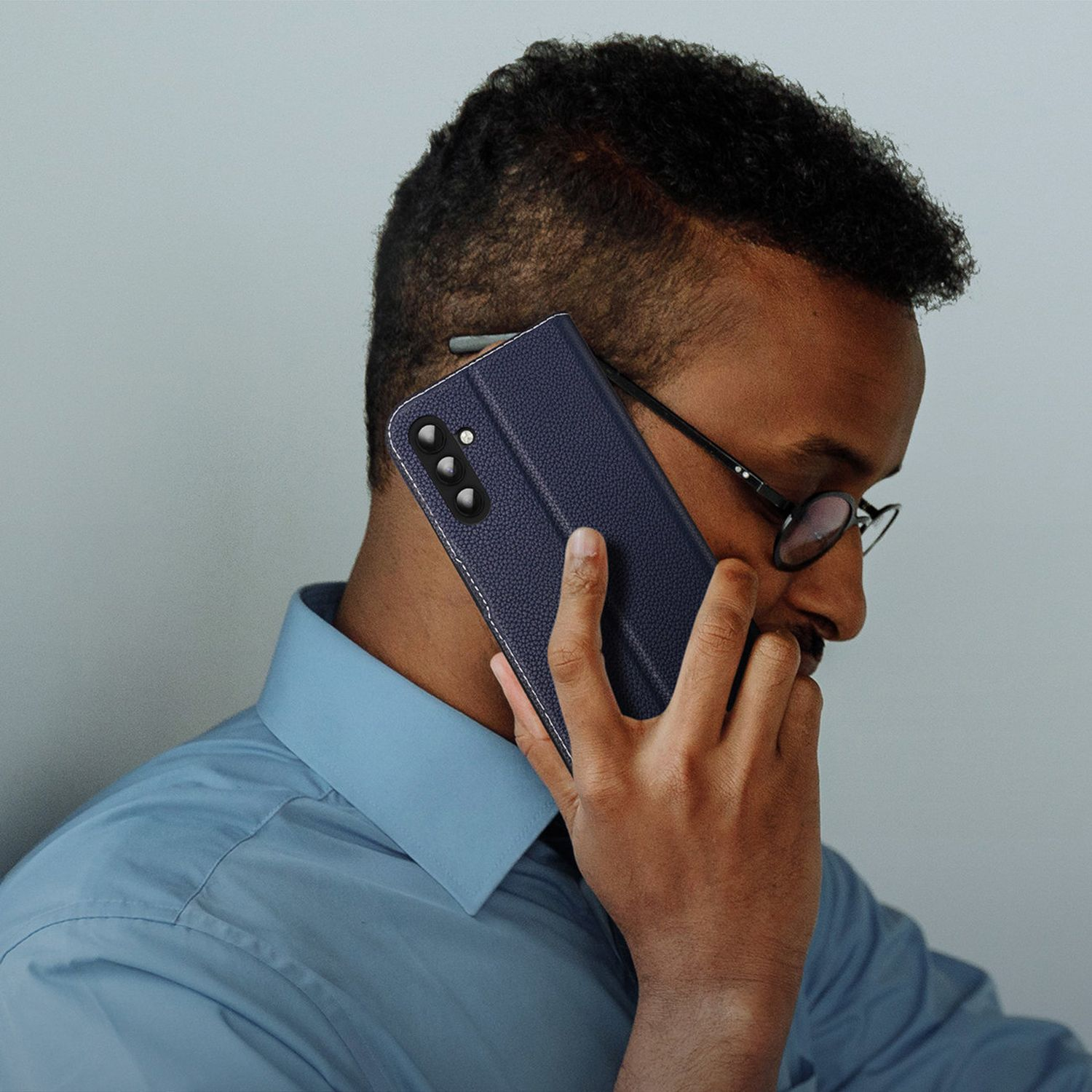 Ein Mann mit Brille, der eine blaue Handyhülle ans Ohr hält und telefoniert.