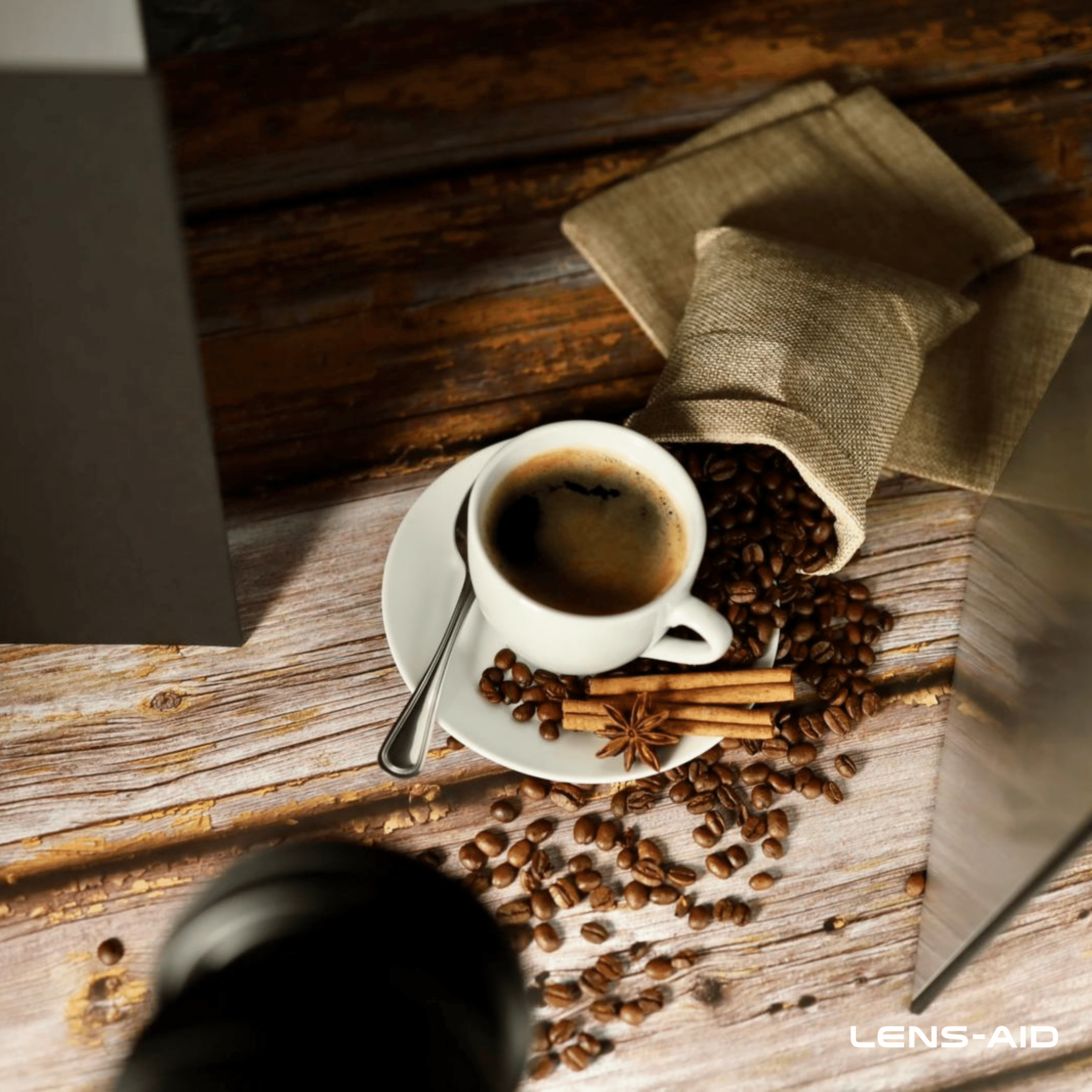 Eine Tasse Kaffee auf einer Untertasse mit Kaffeebohnen, Zimtstangen und einem Anisstern und eine Tüte Kaffeebohnen.