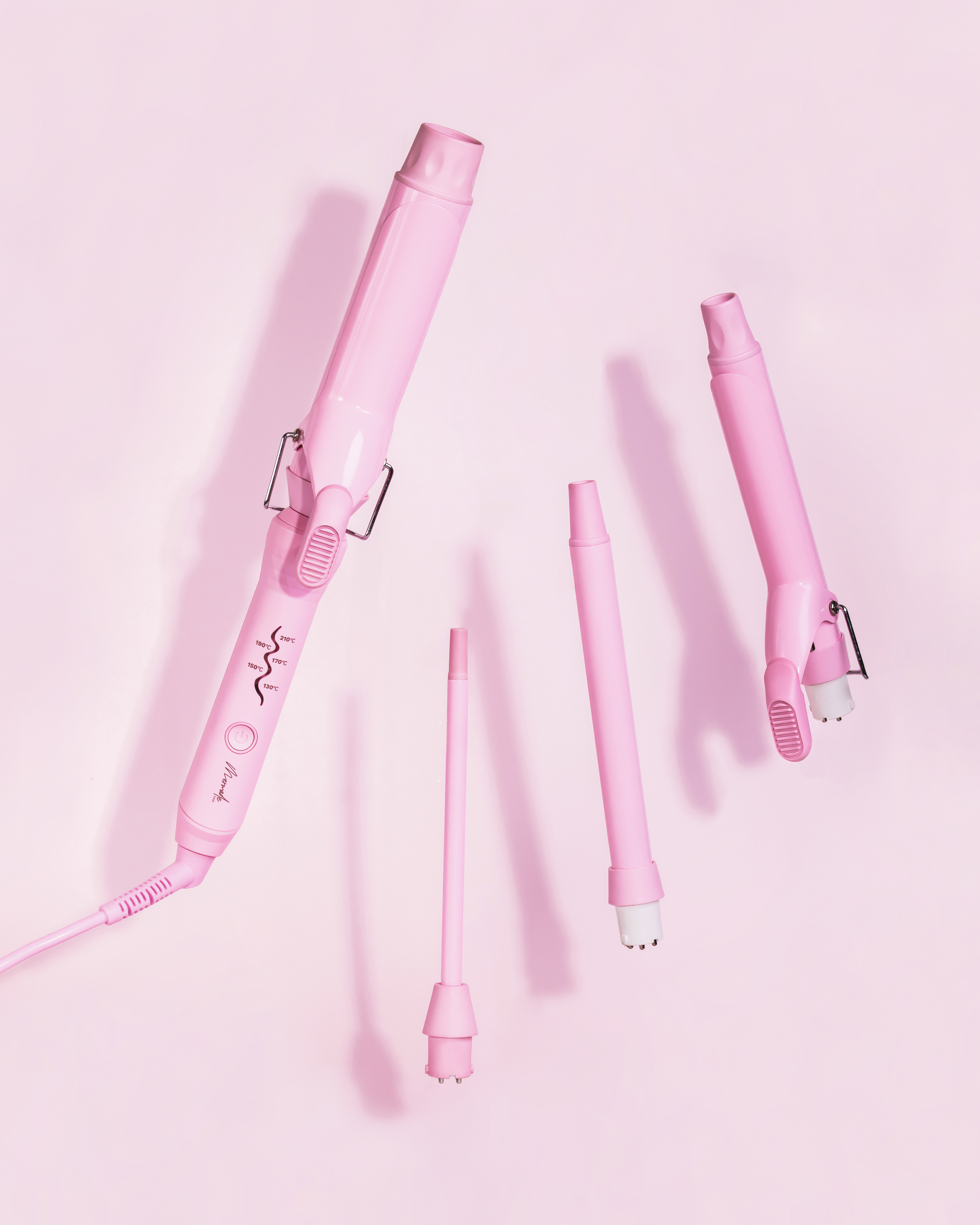 Ein Set rosa Haarstyling-Werkzeuge auf rosa Hintergrund. Werkzeuge umfassen Lockenstäbe und Aufsätze.