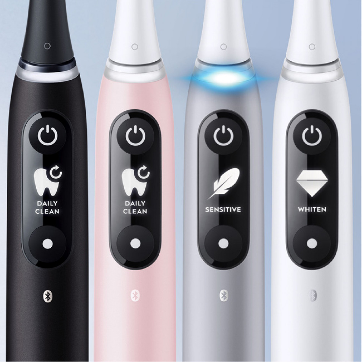 Primo piano di quattro spazzolini elettrici di diversi colori, ciascuno con un pulsante.
