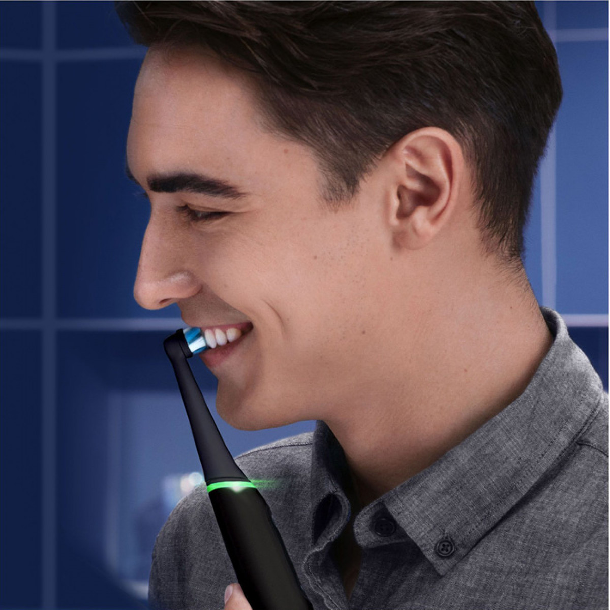 Uomo usa spazzolino elettrico, sorridente. Spazzolino nero con luce verde.