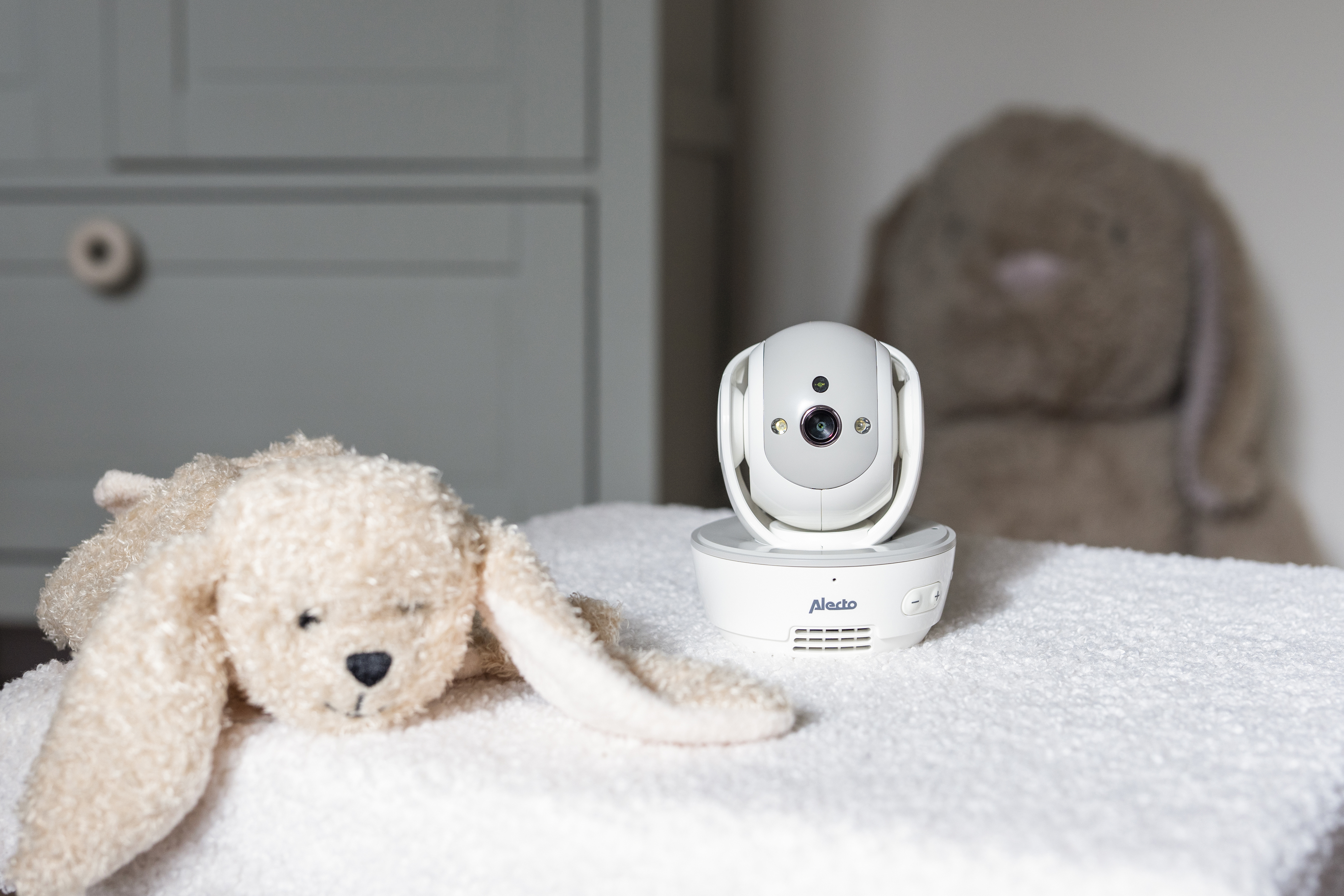 Babyphone mit einem Plüschhasen auf einer weißen Oberfläche vor einer Kommode.