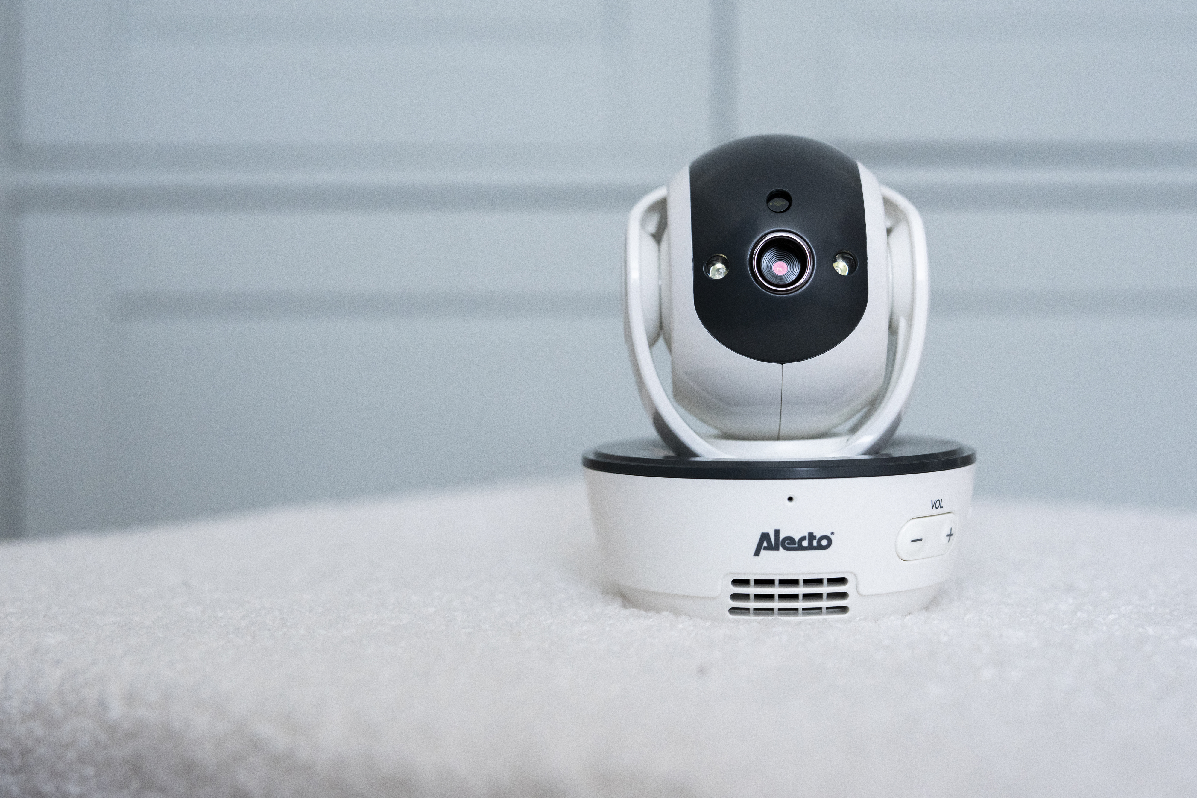 White and black baby monitor camera on a white surface. It has a lens and a round base.