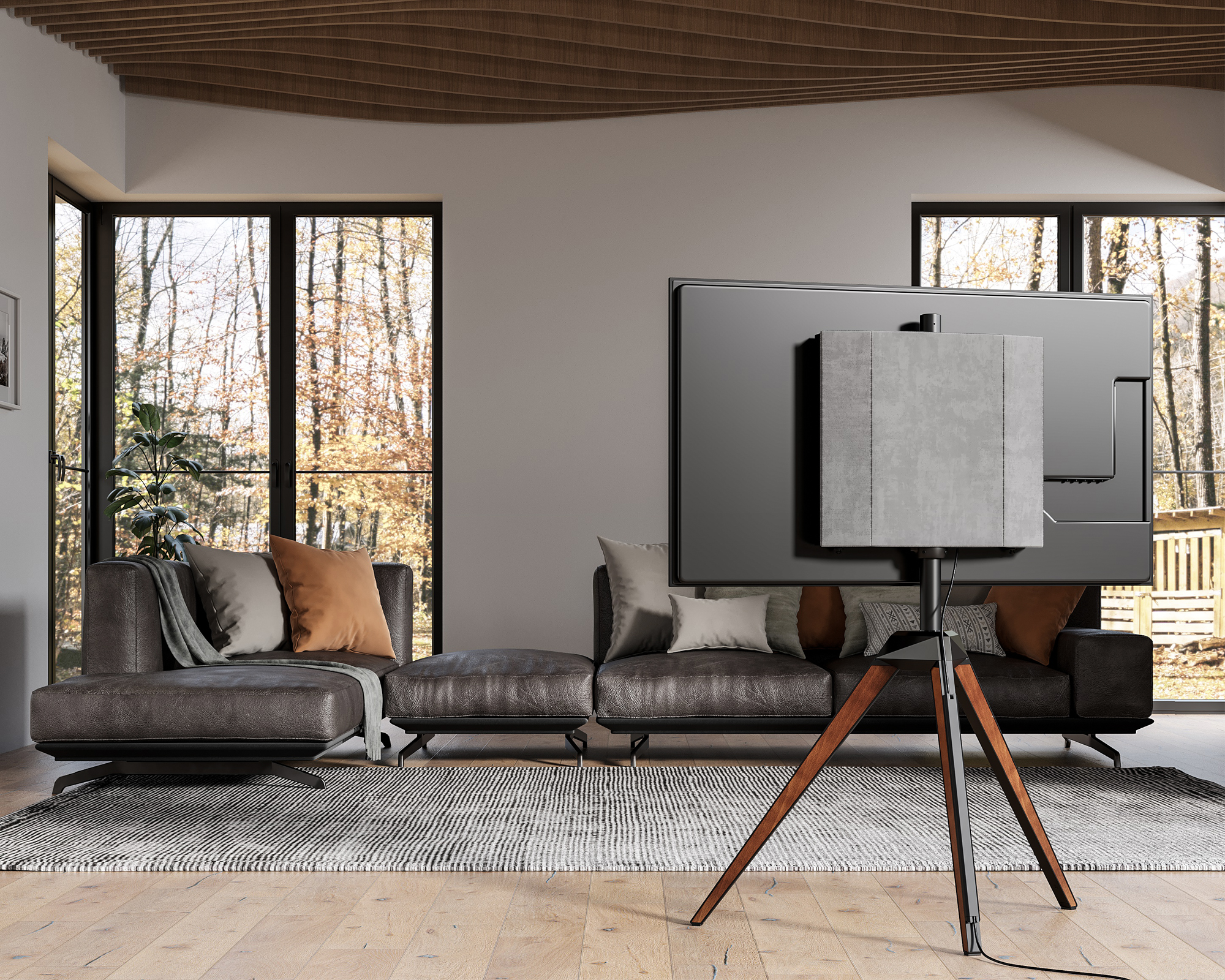 Wohnzimmer mit großem Fernseher auf Holzständer, Ledersofa und Fenstern mit Blick auf einen Wald.