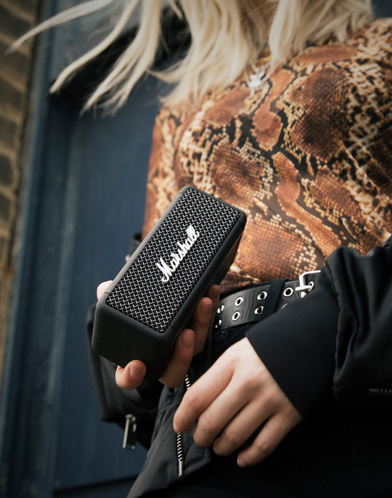 Eine Person hält einen schwarzen Marshall-Lautsprecher. Sie trägt ein Oberteil mit Schlangenmuster.