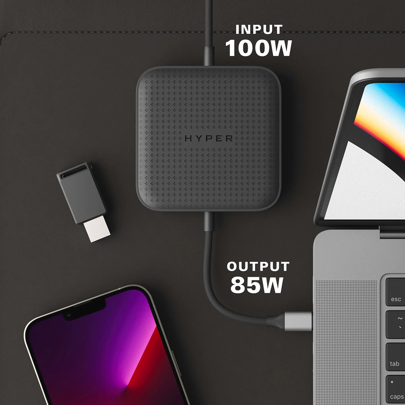 Een zwarte oplaadhub met kabels aangesloten op een telefoon en een laptop. Tekst zegt 'INPUT 100W' en 'OUTPUT 85W'.