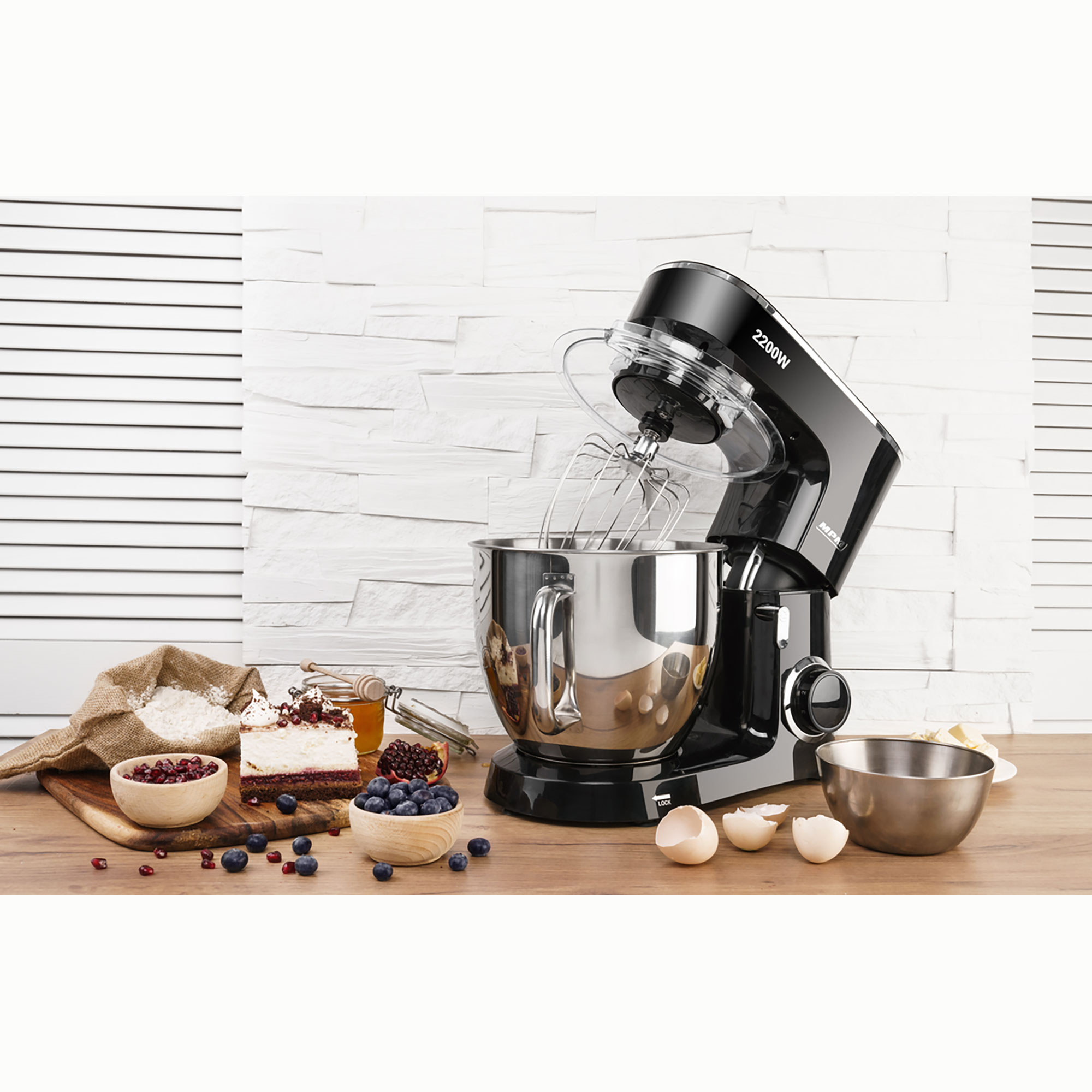 Schwarzer Küchenmixer mit silberner Schüssel und Zubehör auf Holzoberfläche mit Zutaten.