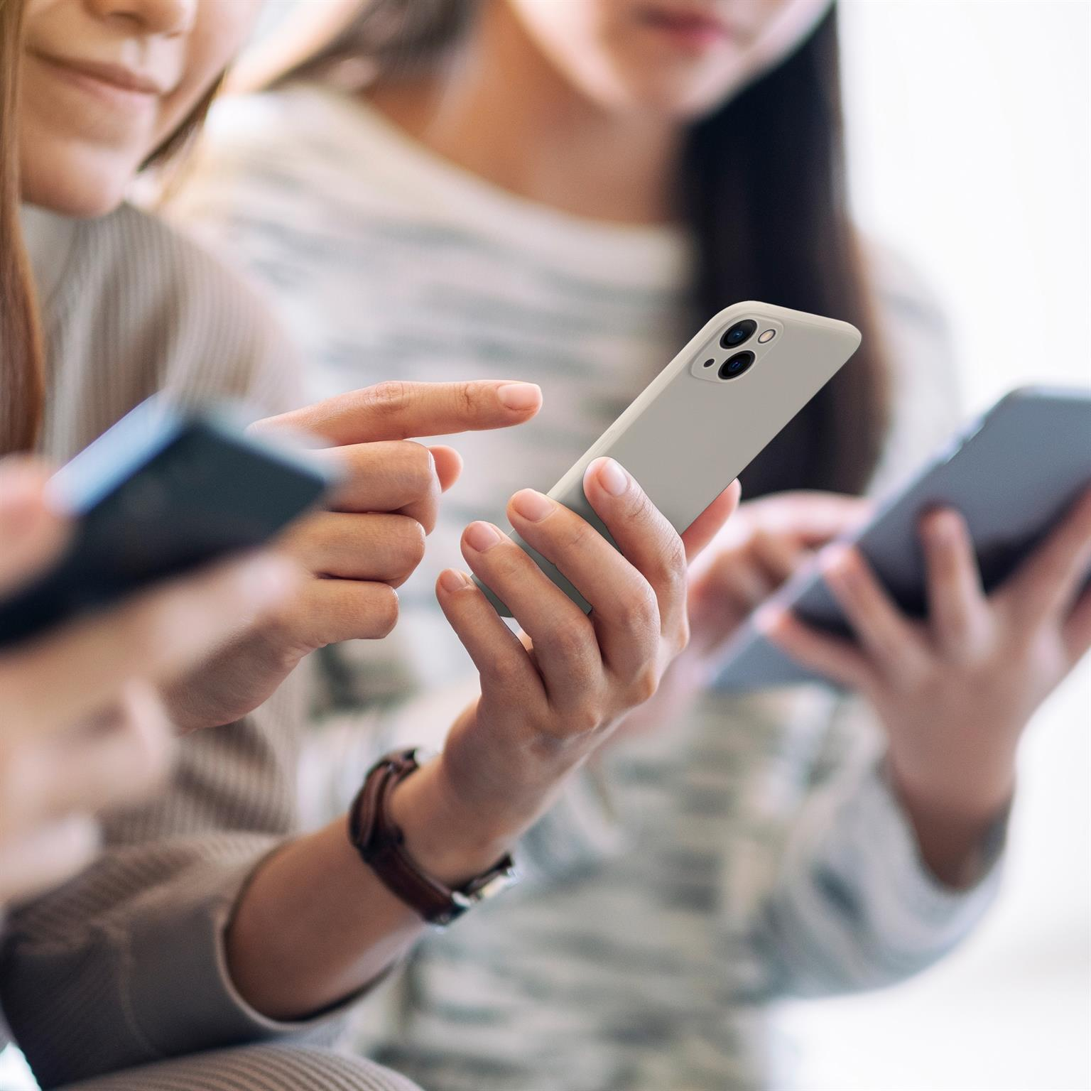 Drei Personen benutzen Smartphones. Eine Person hält ein hellgraues Telefon, eine andere ein dunkleres Telefon.