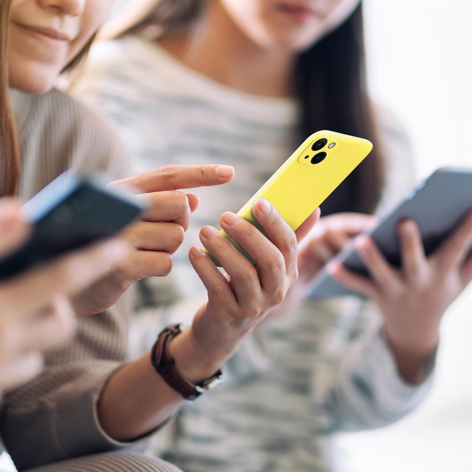 Drei Personen schauen auf Smartphones, eines gelb, zwei dunkelgrau.