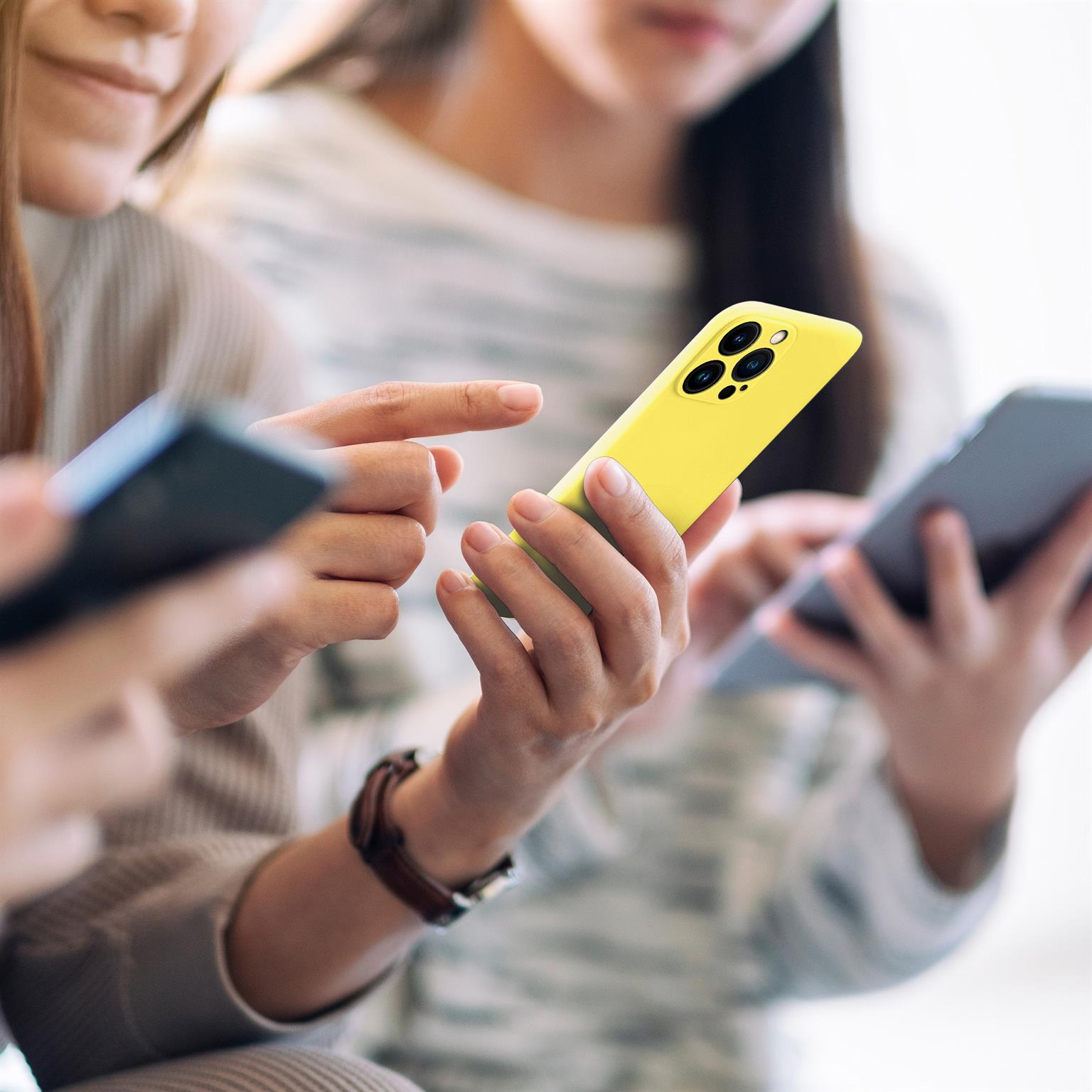 Drei Personen halten Telefone. Ein gelbes Telefon im Fokus, andere unscharf. Weißer Hintergrund.