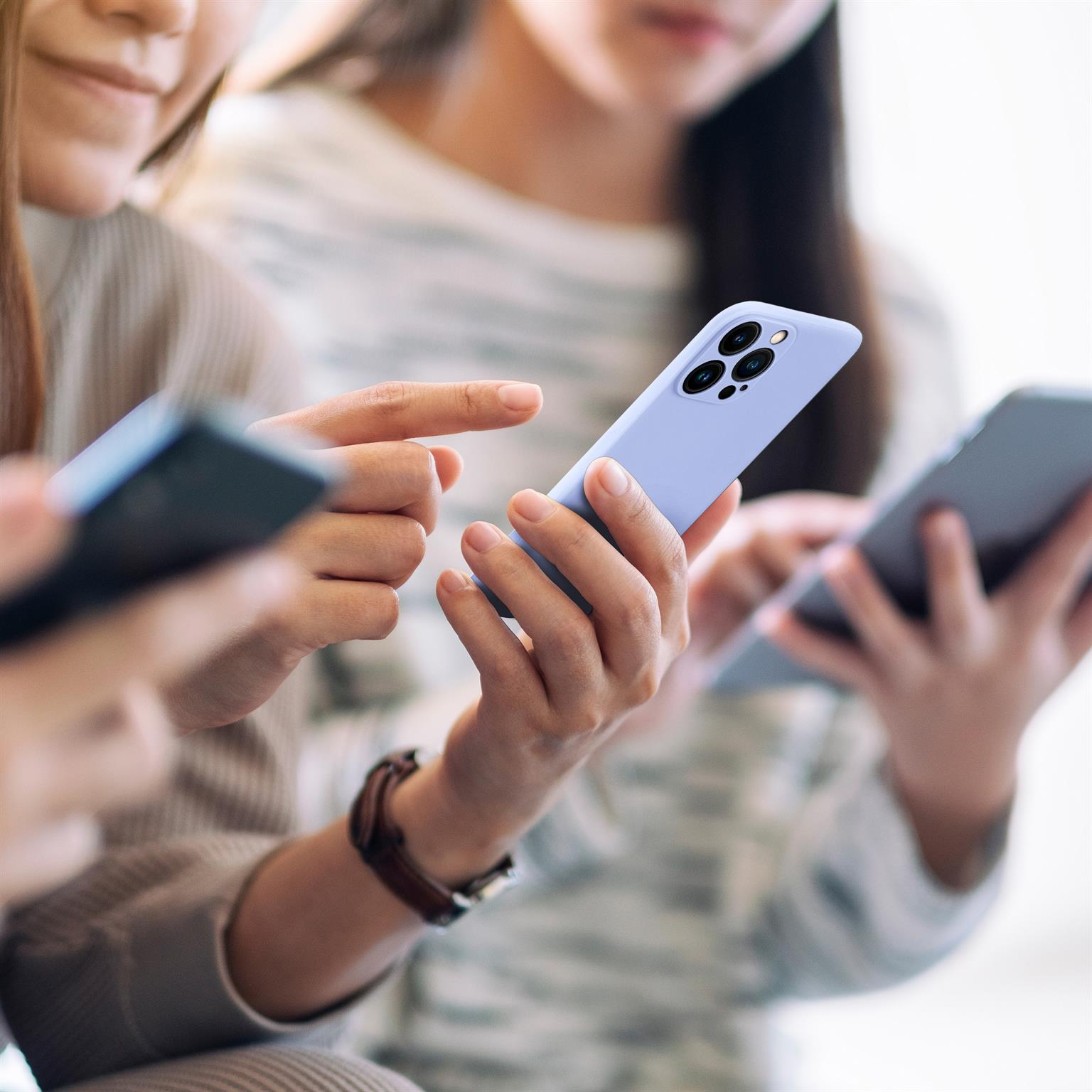 Drei Personen halten Smartphones, ein hellblaues Telefon ist im Fokus.