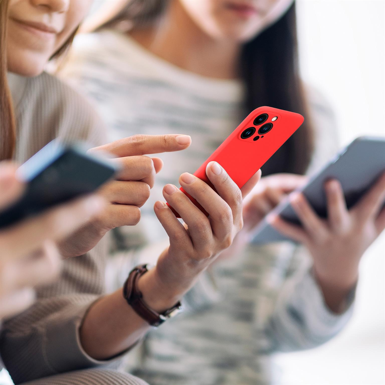 Drei Personen benutzen Smartphones. Eine Person hat eine rote Handyhülle.