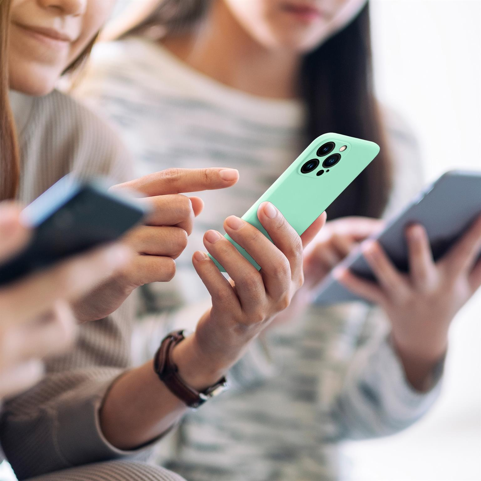 Personen, die Telefone halten. Einer hält ein mintgrünes Telefon, andere verwenden schwarze Telefone. Unscharfer Hintergrund.