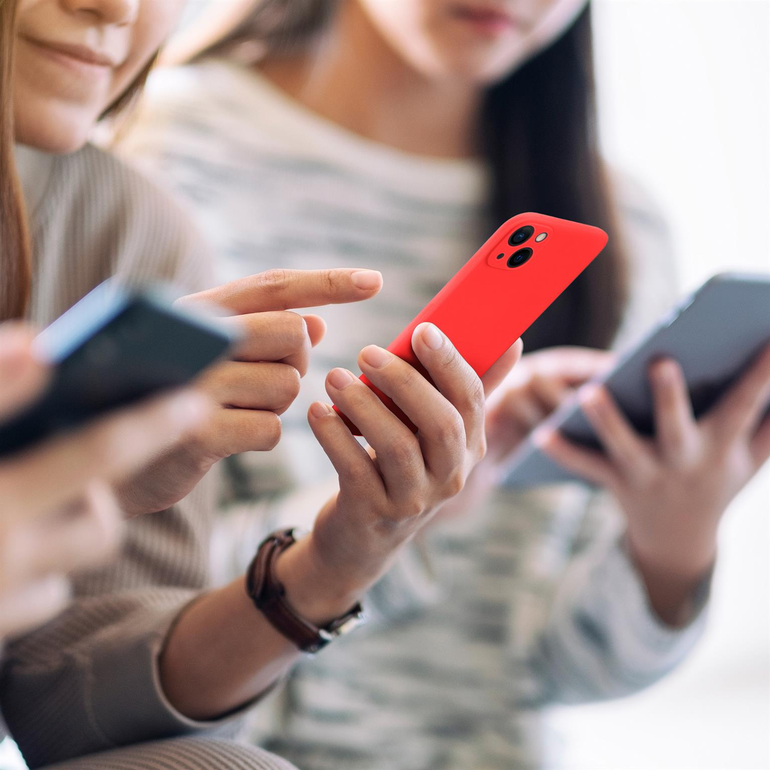 Drei Personen halten Telefone. Eine Person hält ein rotes Telefon. Die anderen beiden halten dunkelgraue Telefone.