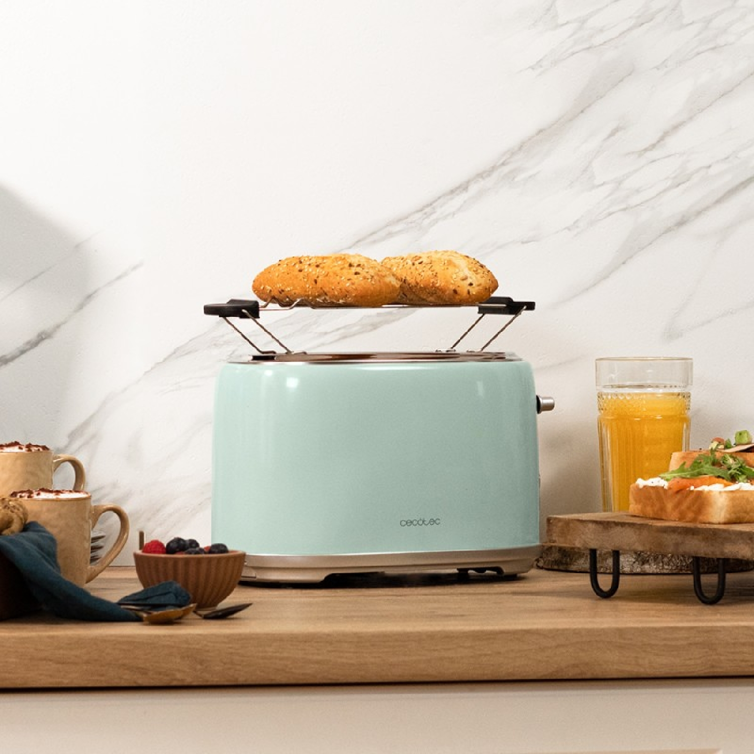 Toaster with two buns on top. Mint green color. Wooden surface, white marble background.