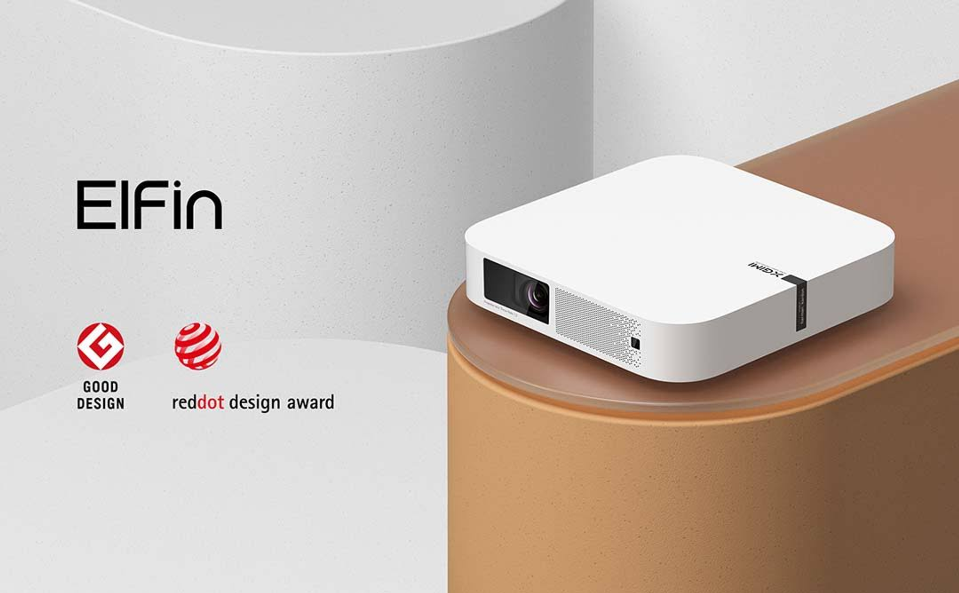 Weißer Projektor auf brauner Oberfläche. Mit ElFin beschriftet und mit Good Design- und Red Dot-Auszeichnungen.